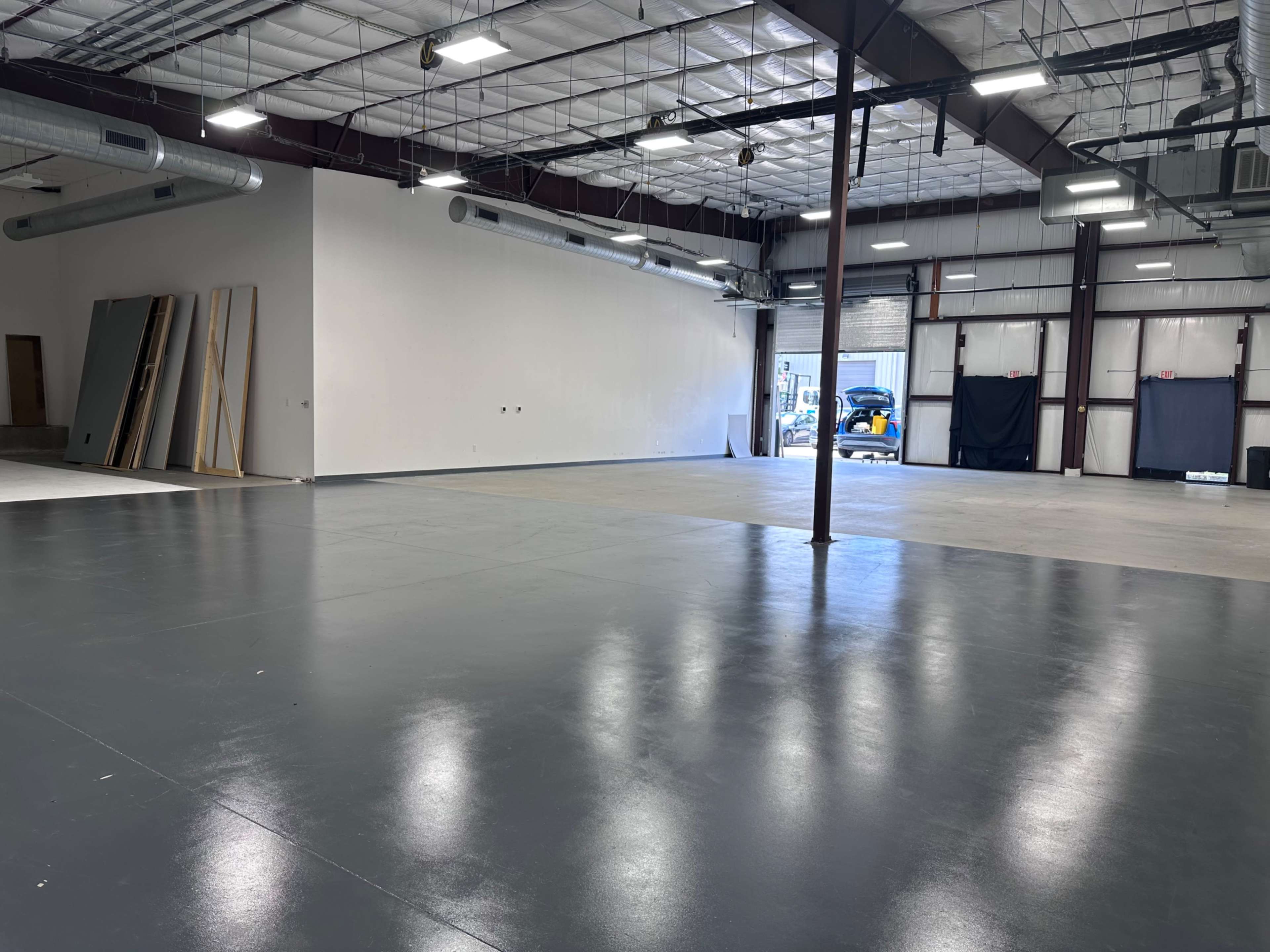 The image shows a large, empty industrial space with a polished floor, exposed metal beams, and a roll-up door in the background.