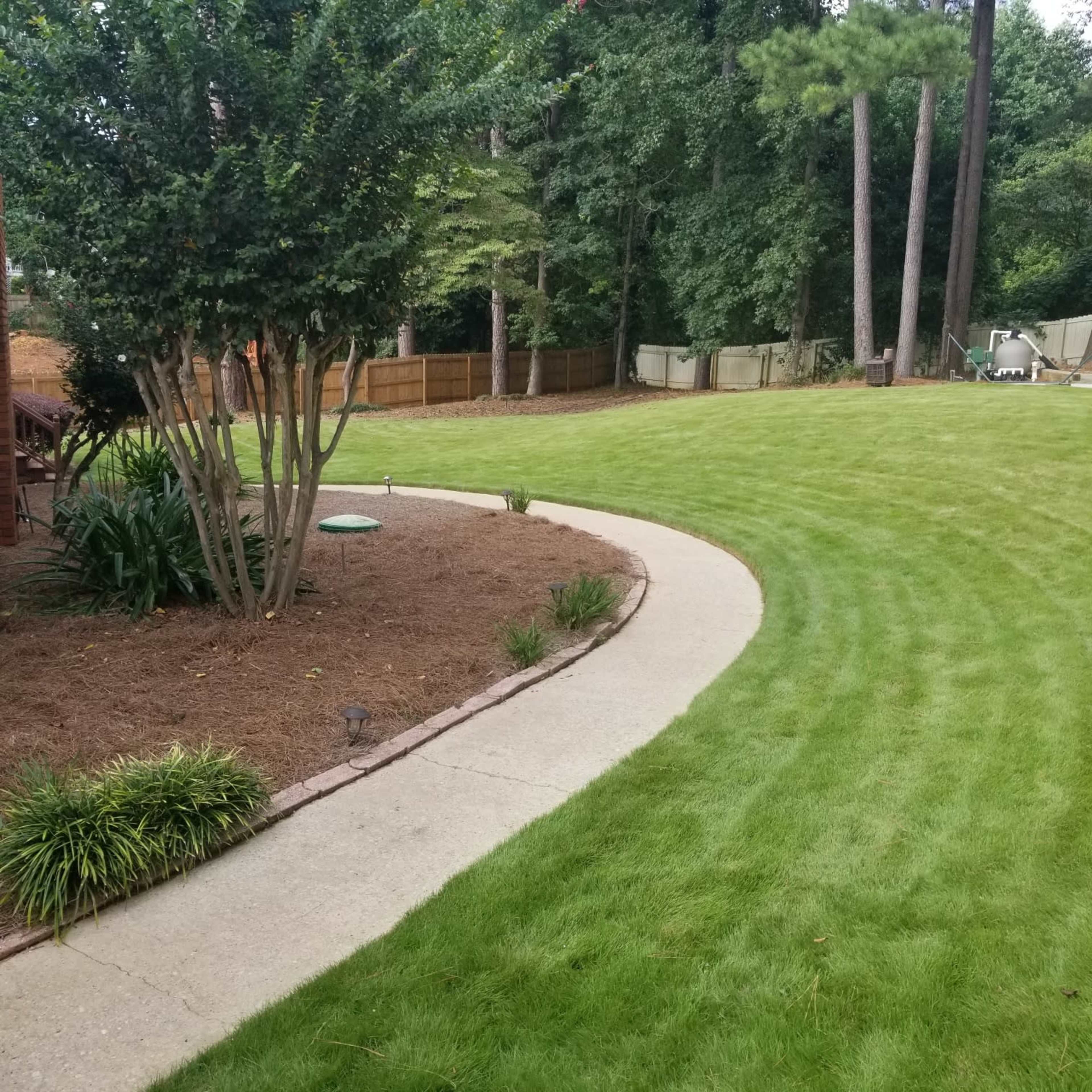 A curved concrete pathway winds through a neatly trimmed lawn surrounded by trees and shrubs.