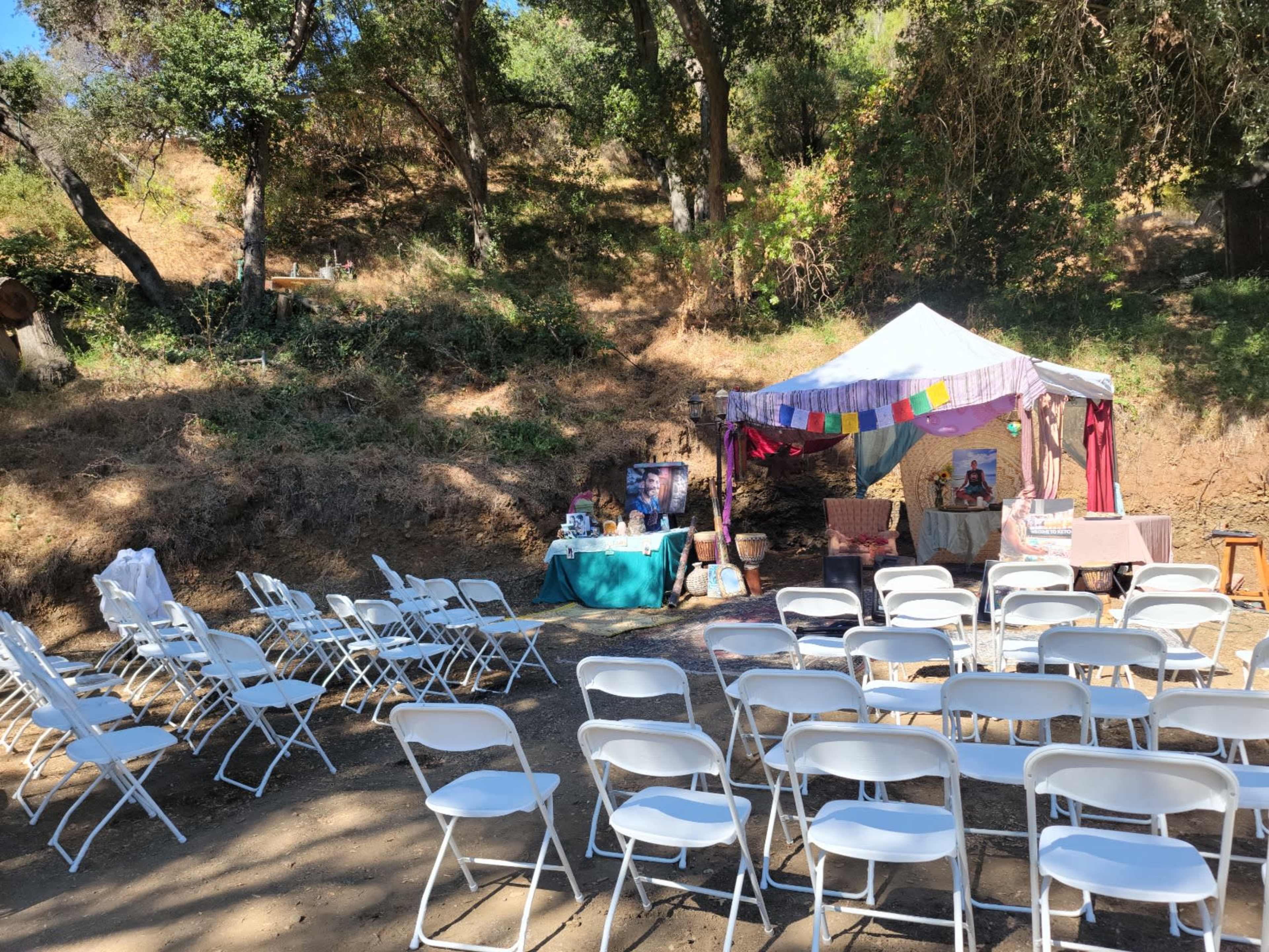 A setup for an outdoor event features a white tent with colorful decorations and seating arranged in rows.