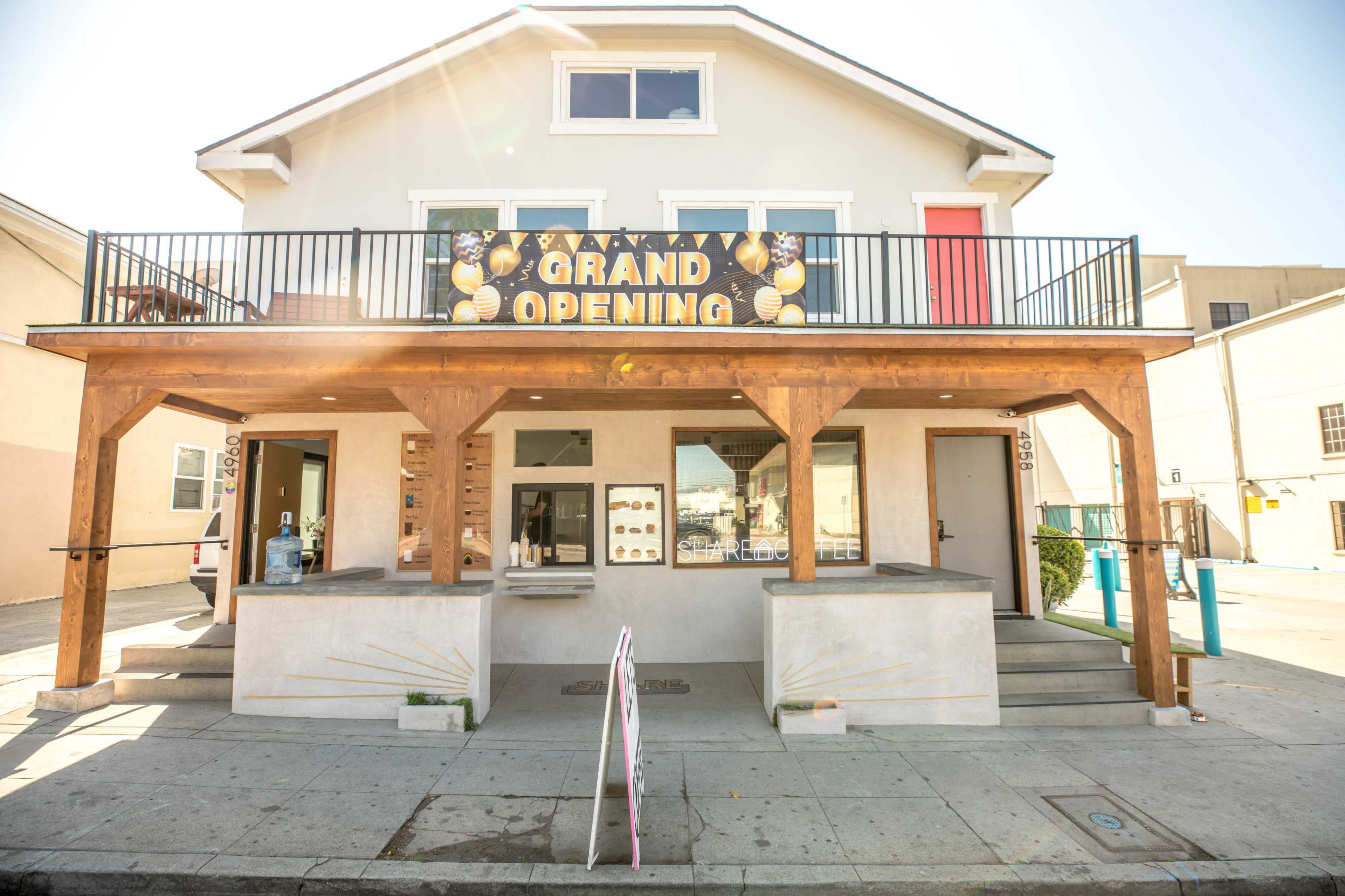 A two-story building with a wooden porch displays a large sign announcing a grand opening.