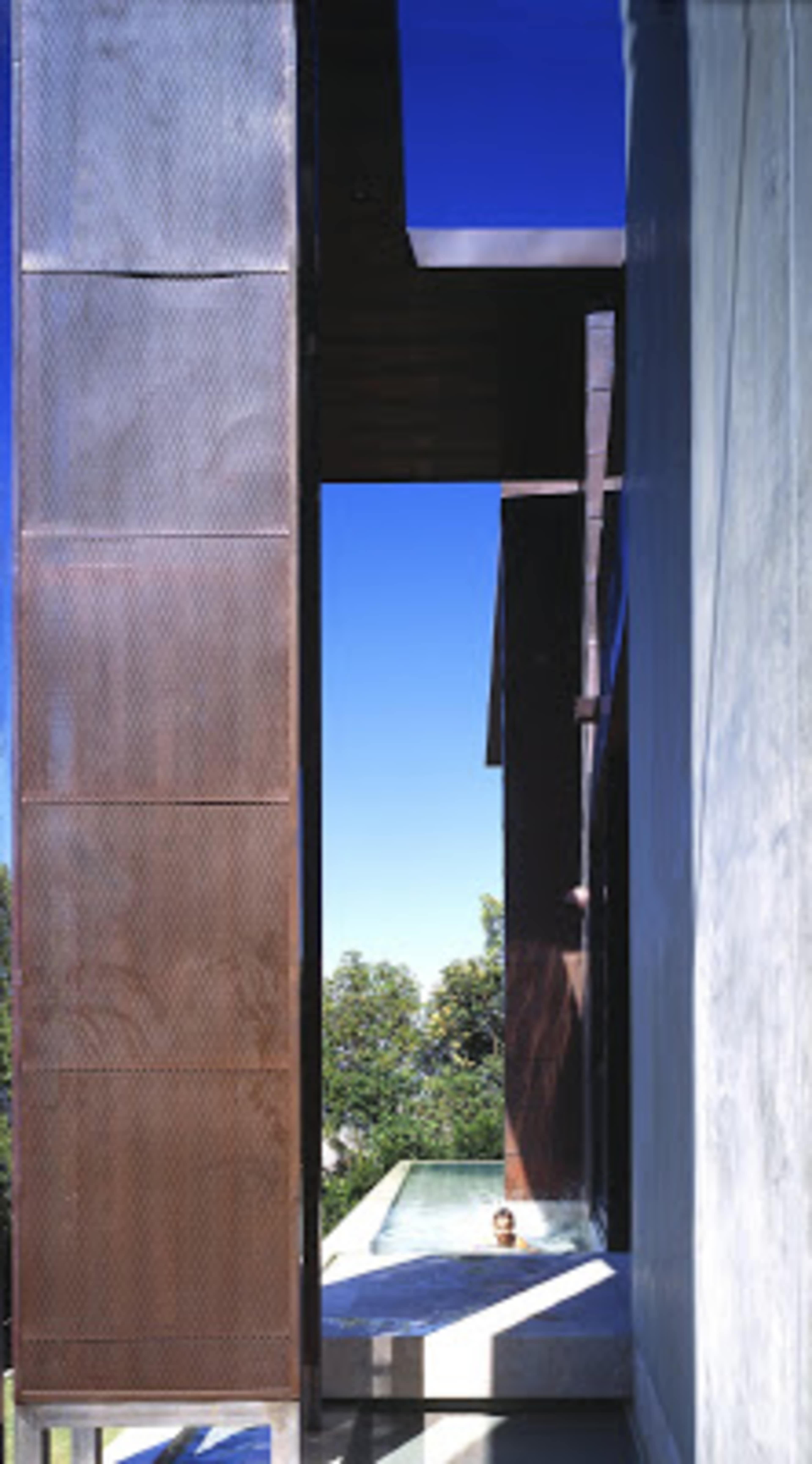 A modern architectural structure with a narrow pathway leading to a pool, framed by tall, metallic panels.