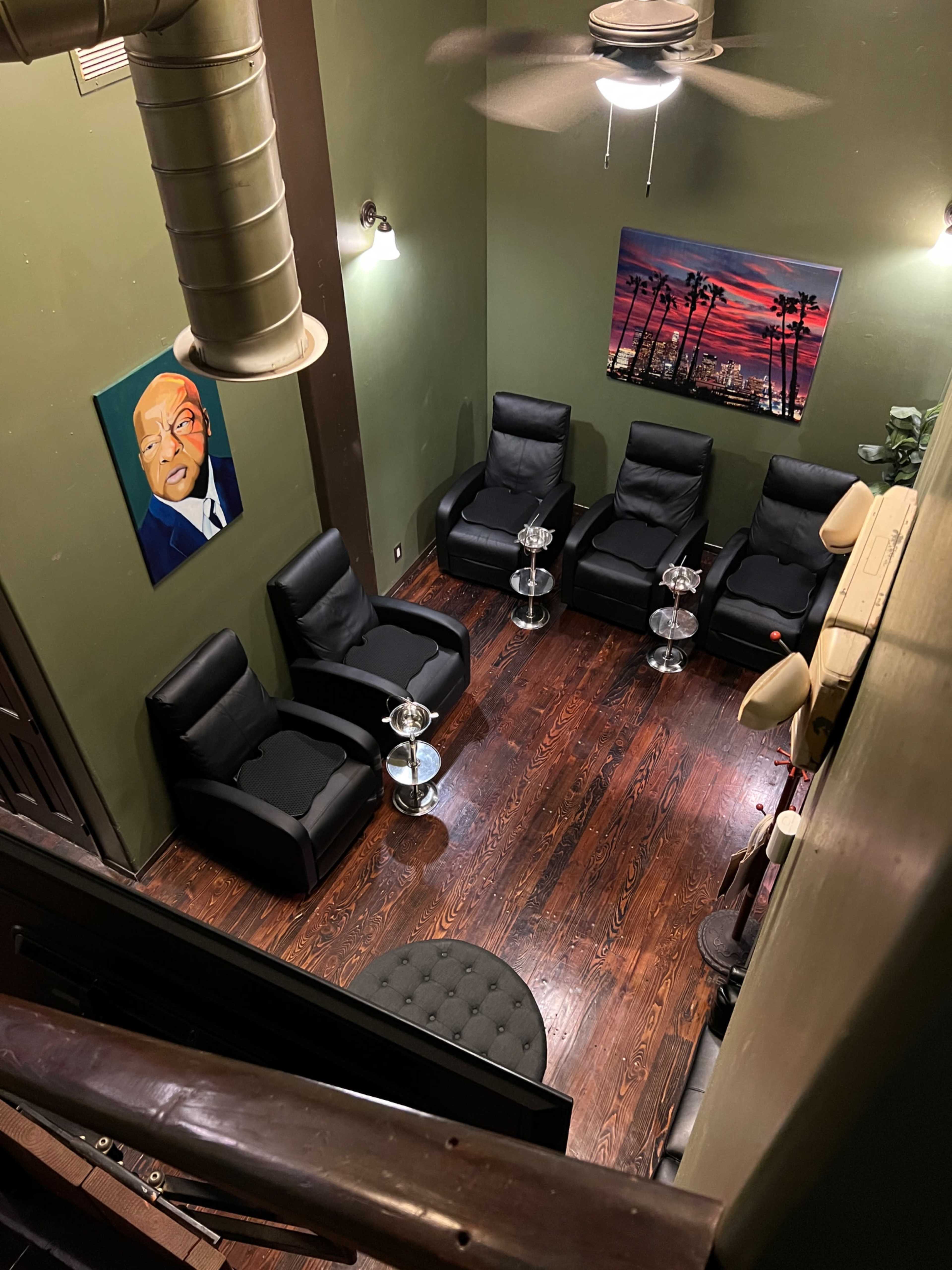 A seating area with six black chairs arranged around two glass coffee tables, set in a room with green walls and wooden flooring.