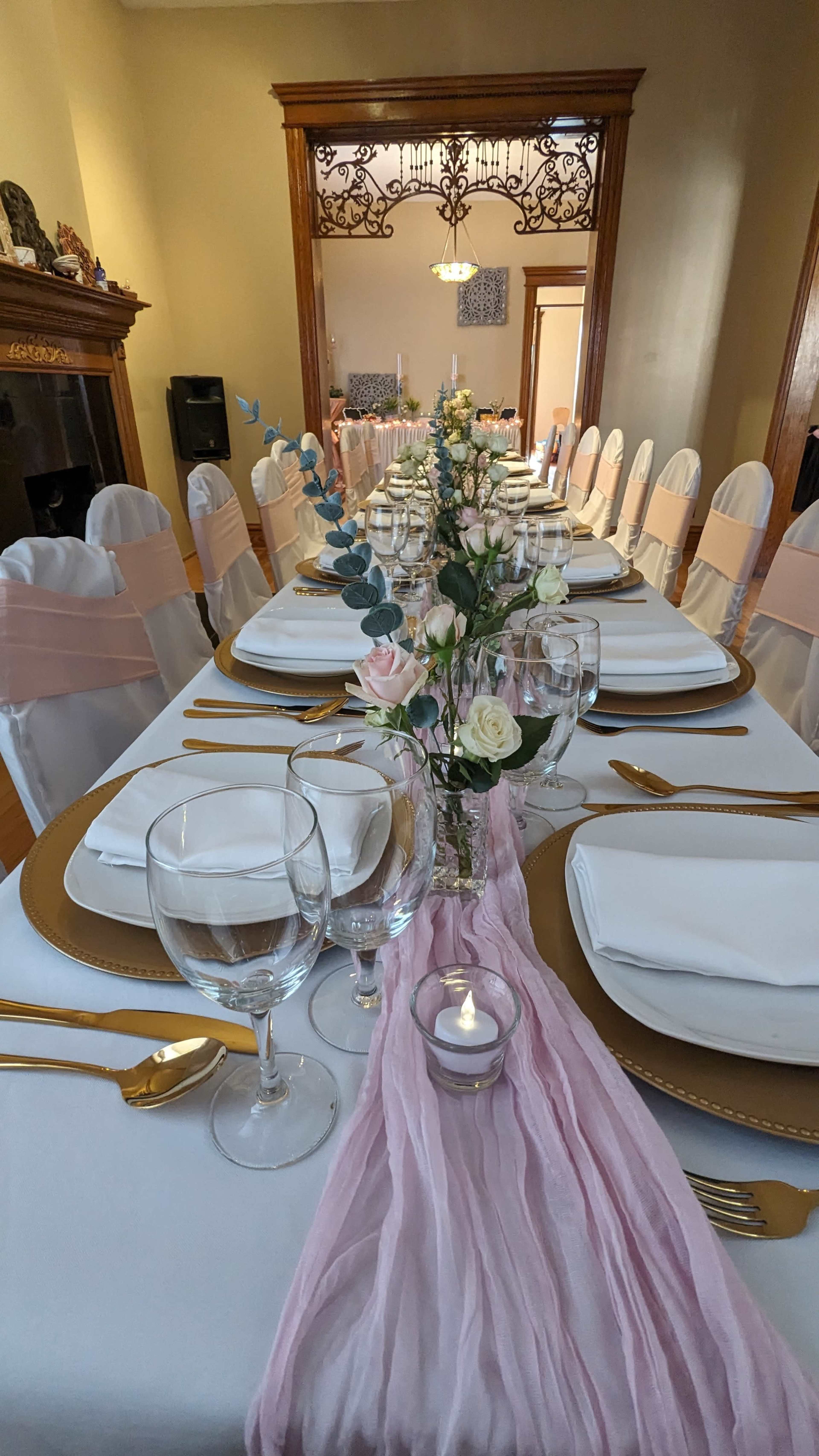 A long banquet table is set with white plates, gold chargers, and floral centerpieces under soft lighting in a room with an elegant decor.