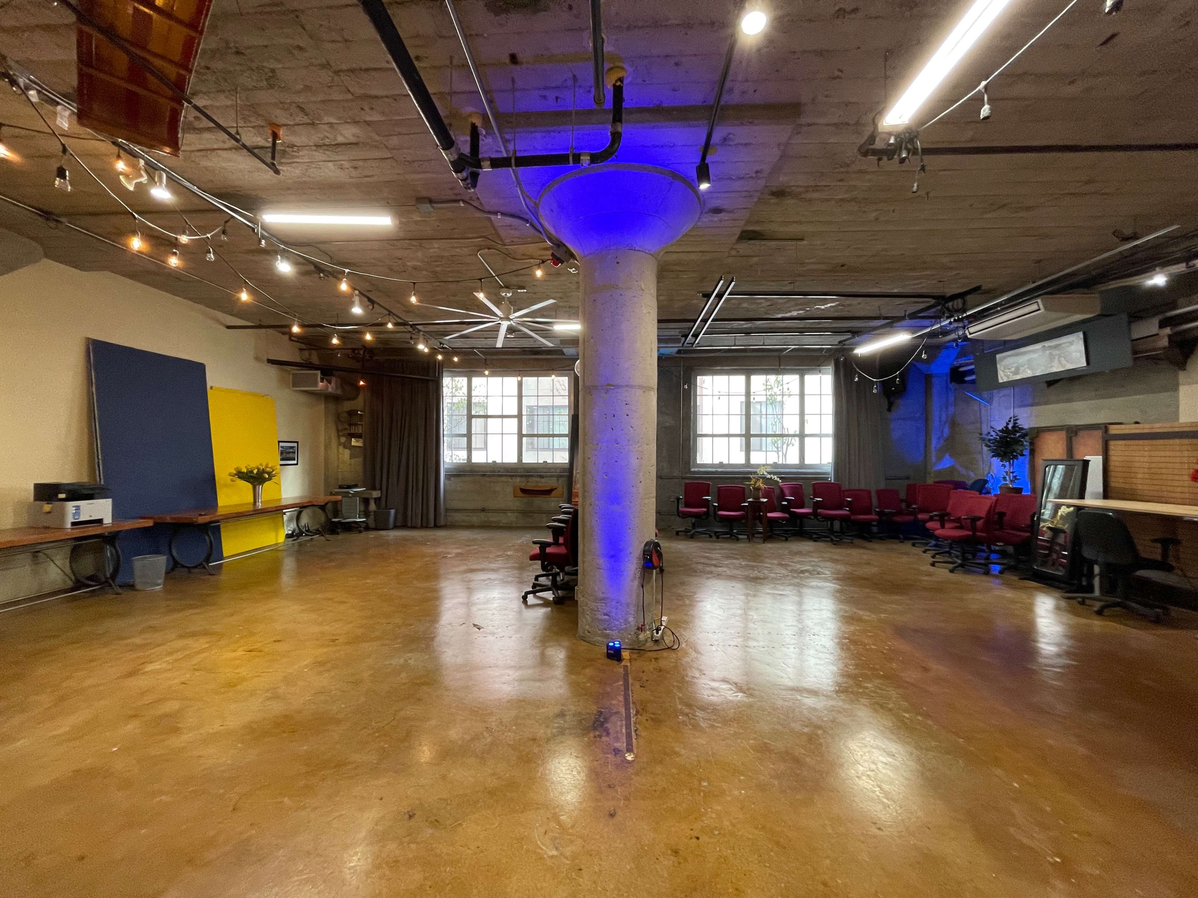 A spacious, industrial-style room with polished concrete floors, a central column, and red chairs arranged around a corner.
