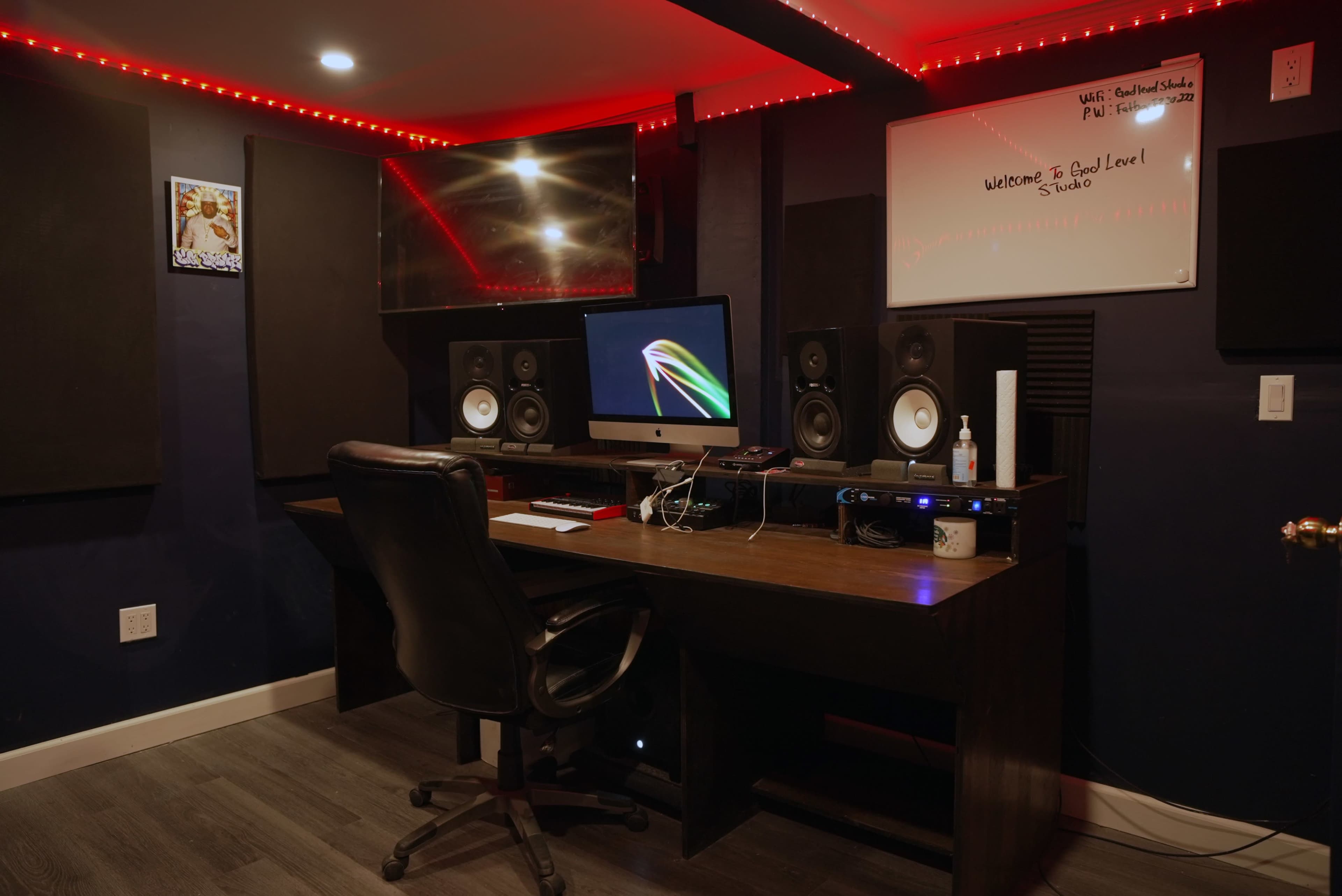 A dimly lit recording studio with a desk, a computer, and audio equipment, surrounded by soundproof panels and illuminated by red LED lights.