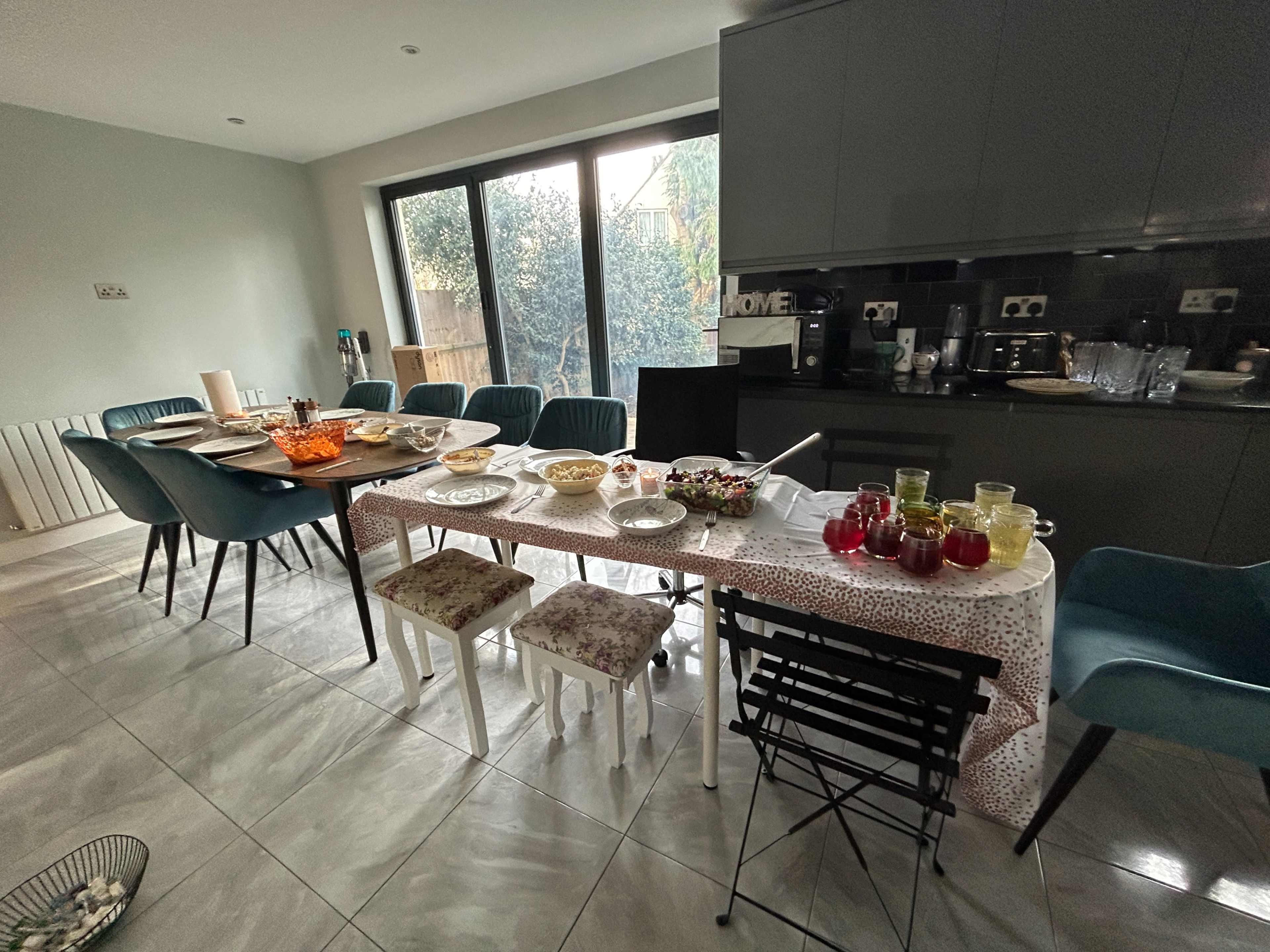 A dining table set with various dishes and drinks is surrounded by chairs in a modern kitchen.