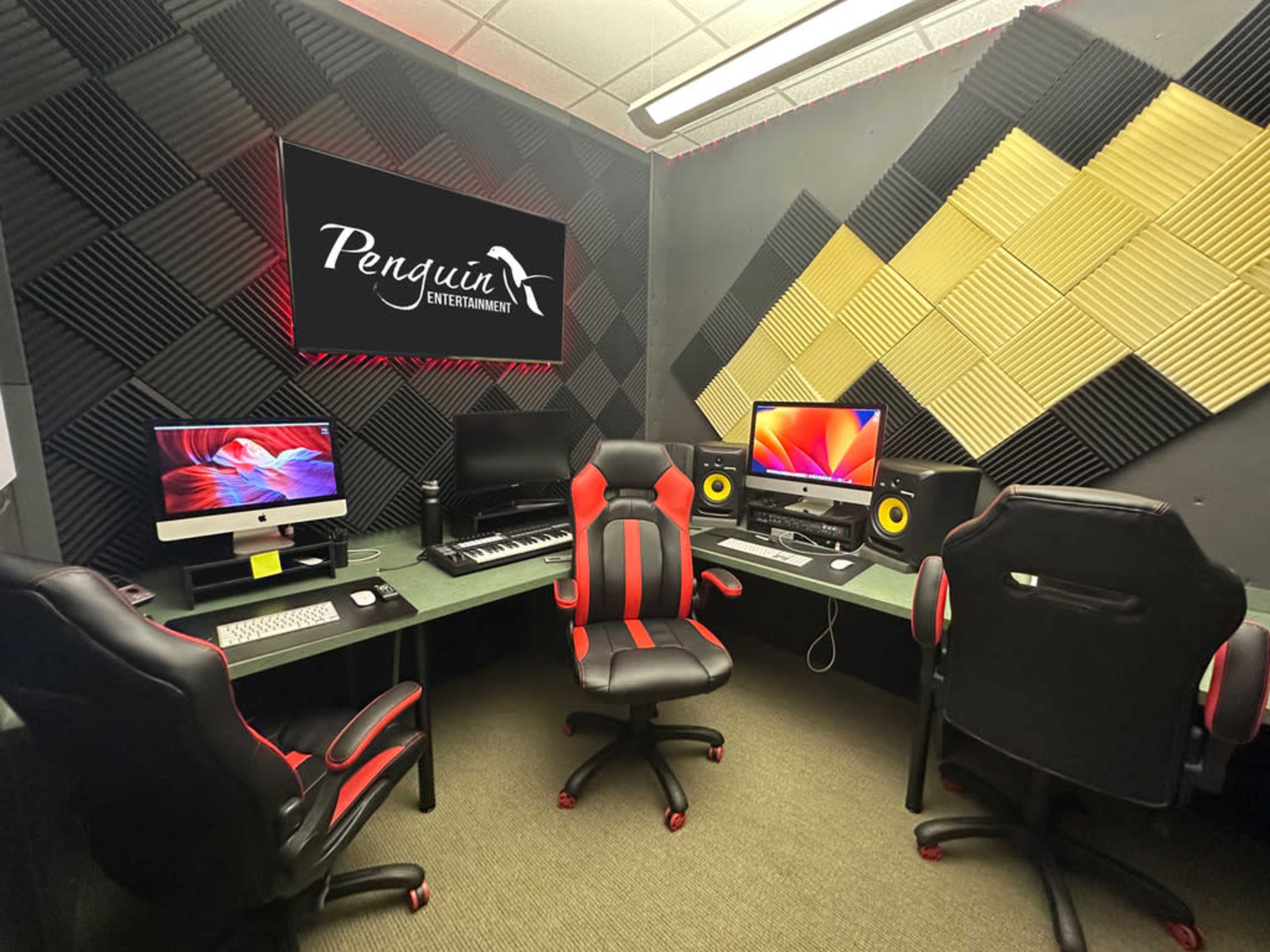 A music production studio featuring three workstations with computers, keyboards, and studio monitors, surrounded by sound-absorbing wall panels.