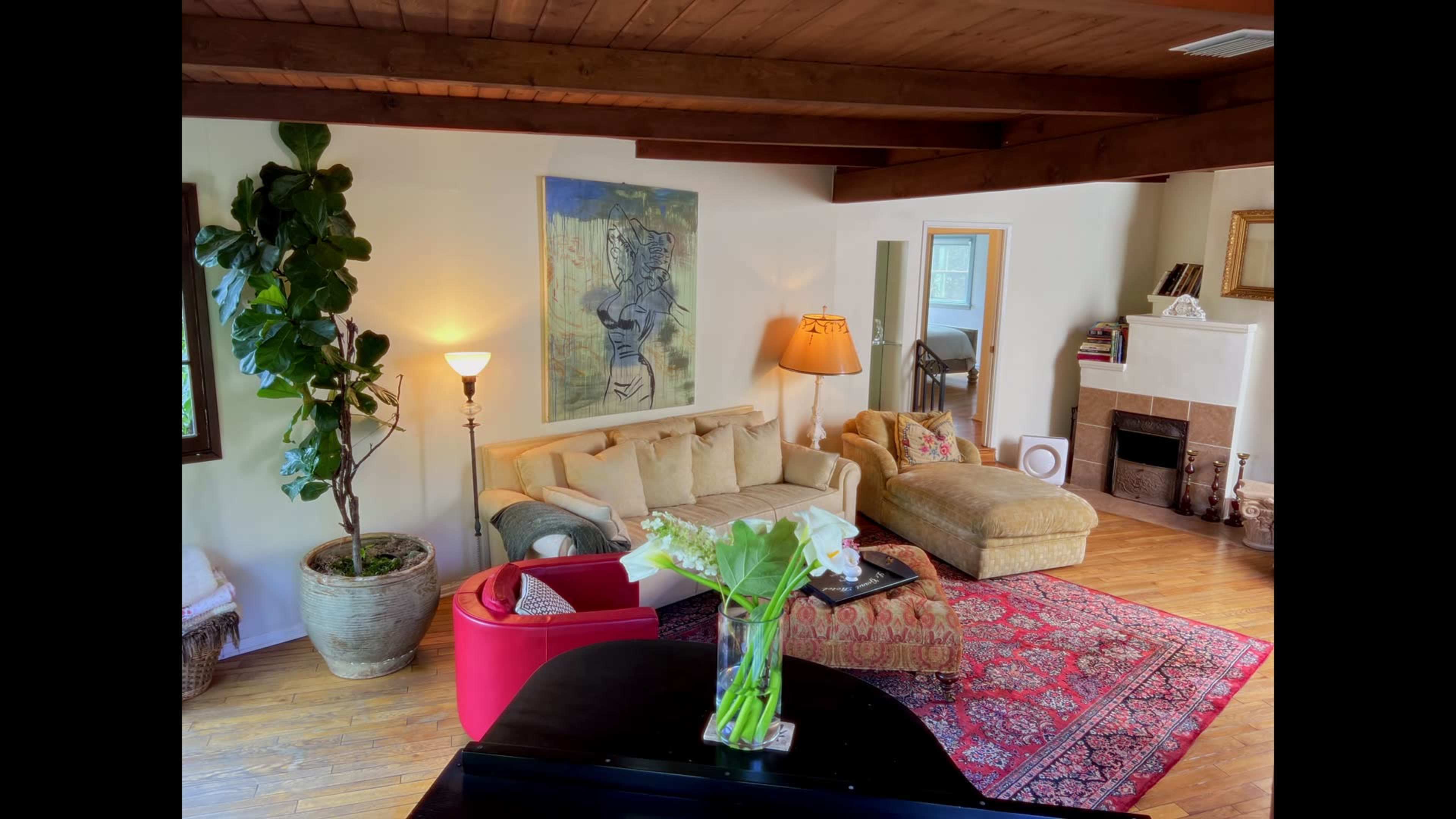 The image shows a living room with a beige sofa, an armchair, a large painting on the wall, and a piano in the foreground.