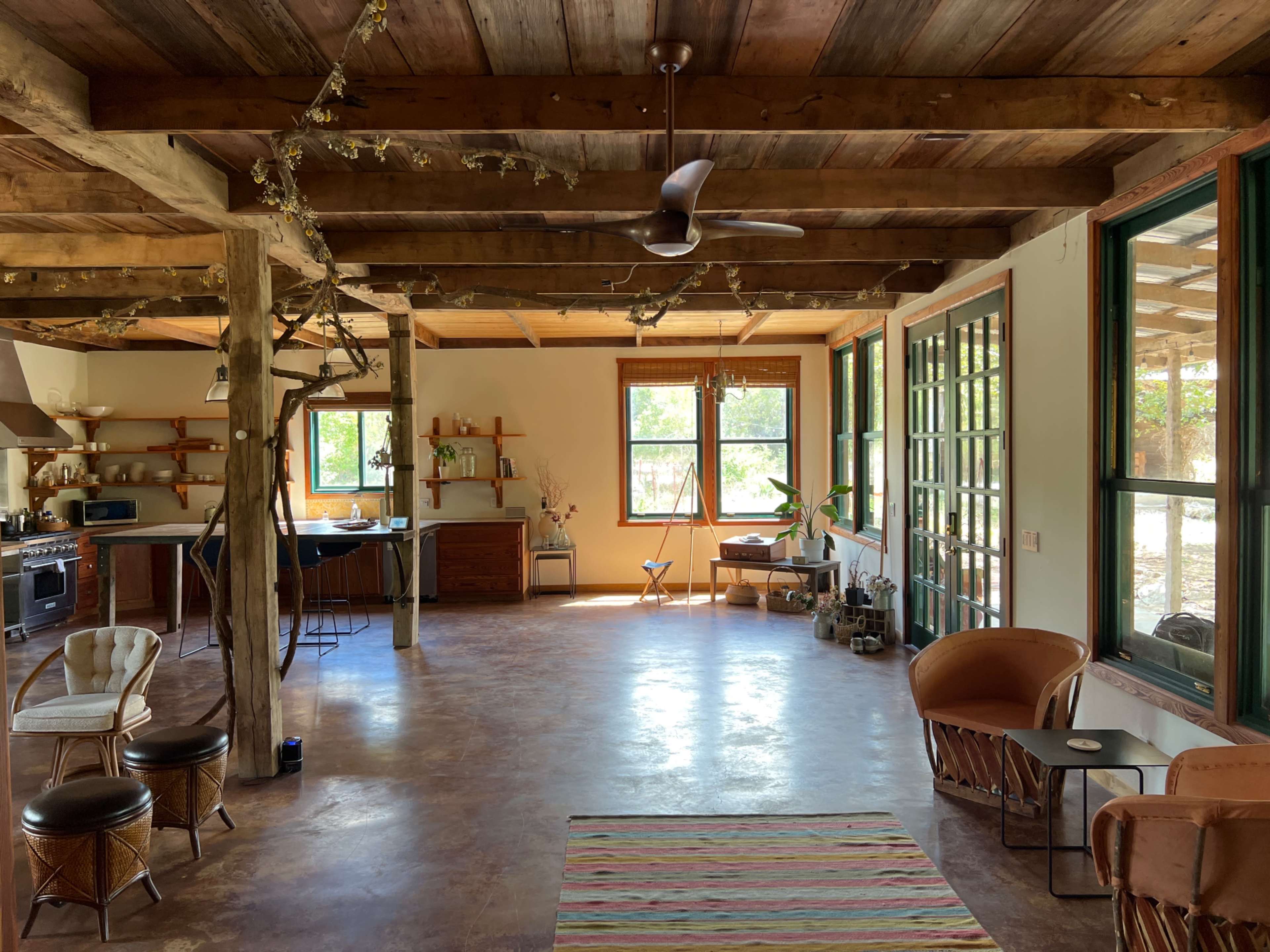 A spacious, open-concept living area with wooden beams, large windows, and minimalist furnishings.