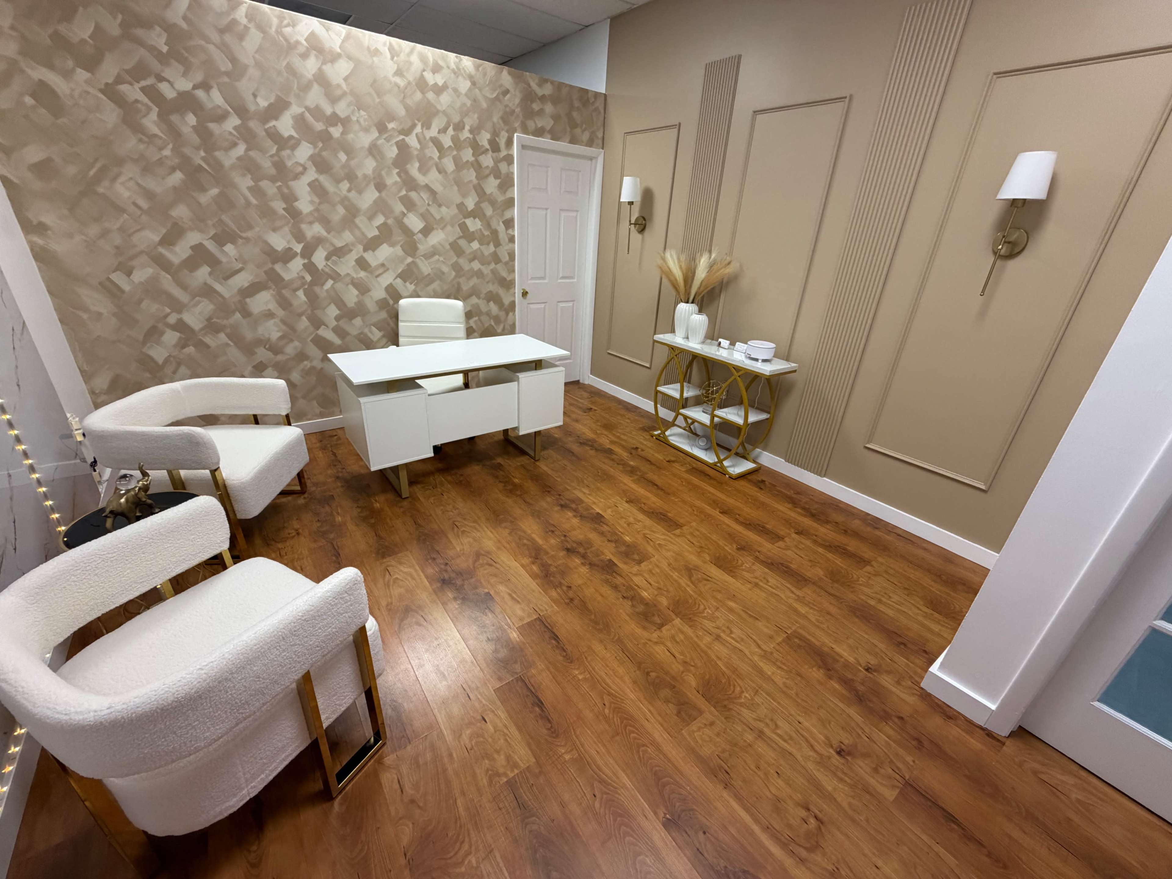 The image shows a modern office interior featuring a desk, two white chairs, and decorative wall elements in neutral tones.