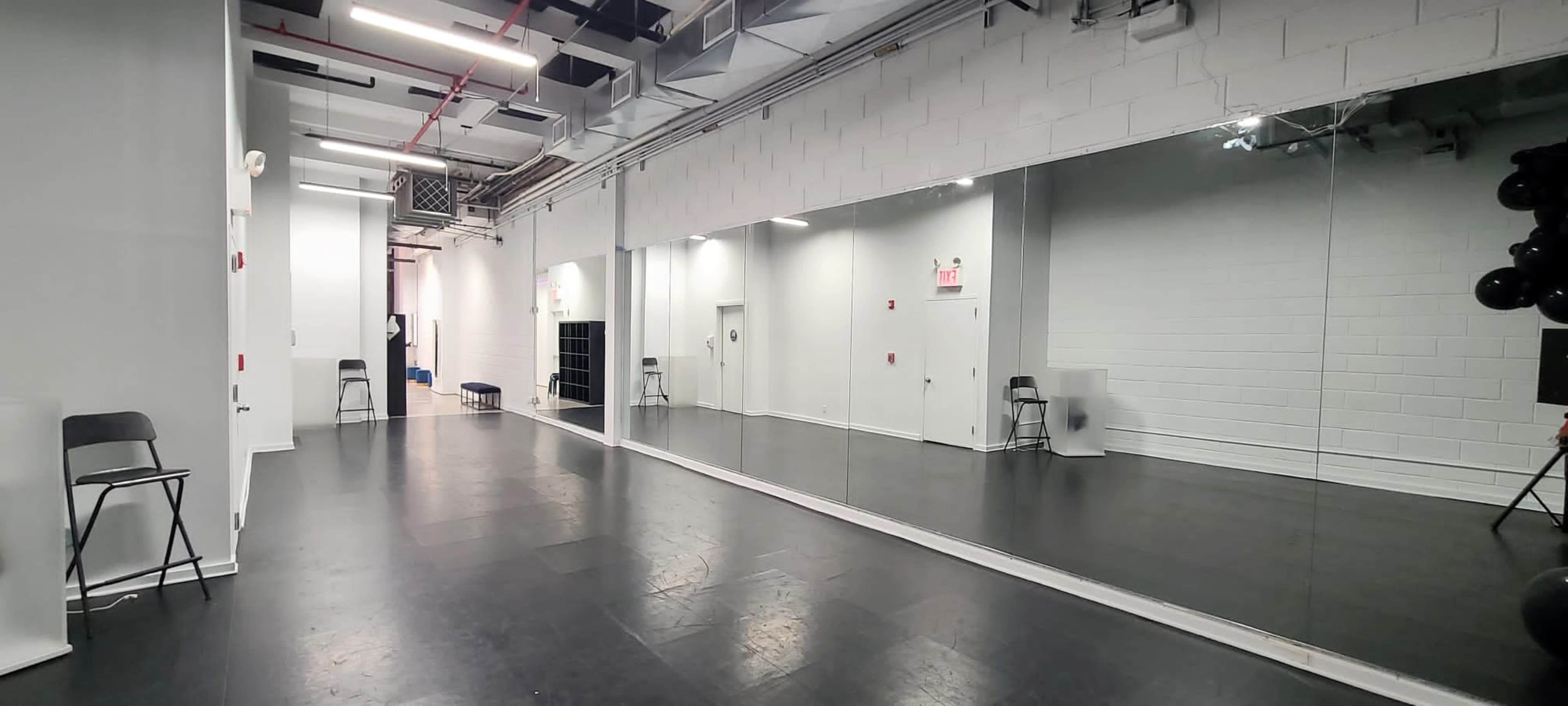 A spacious, empty dance studio featuring a large mirrored wall and black flooring.