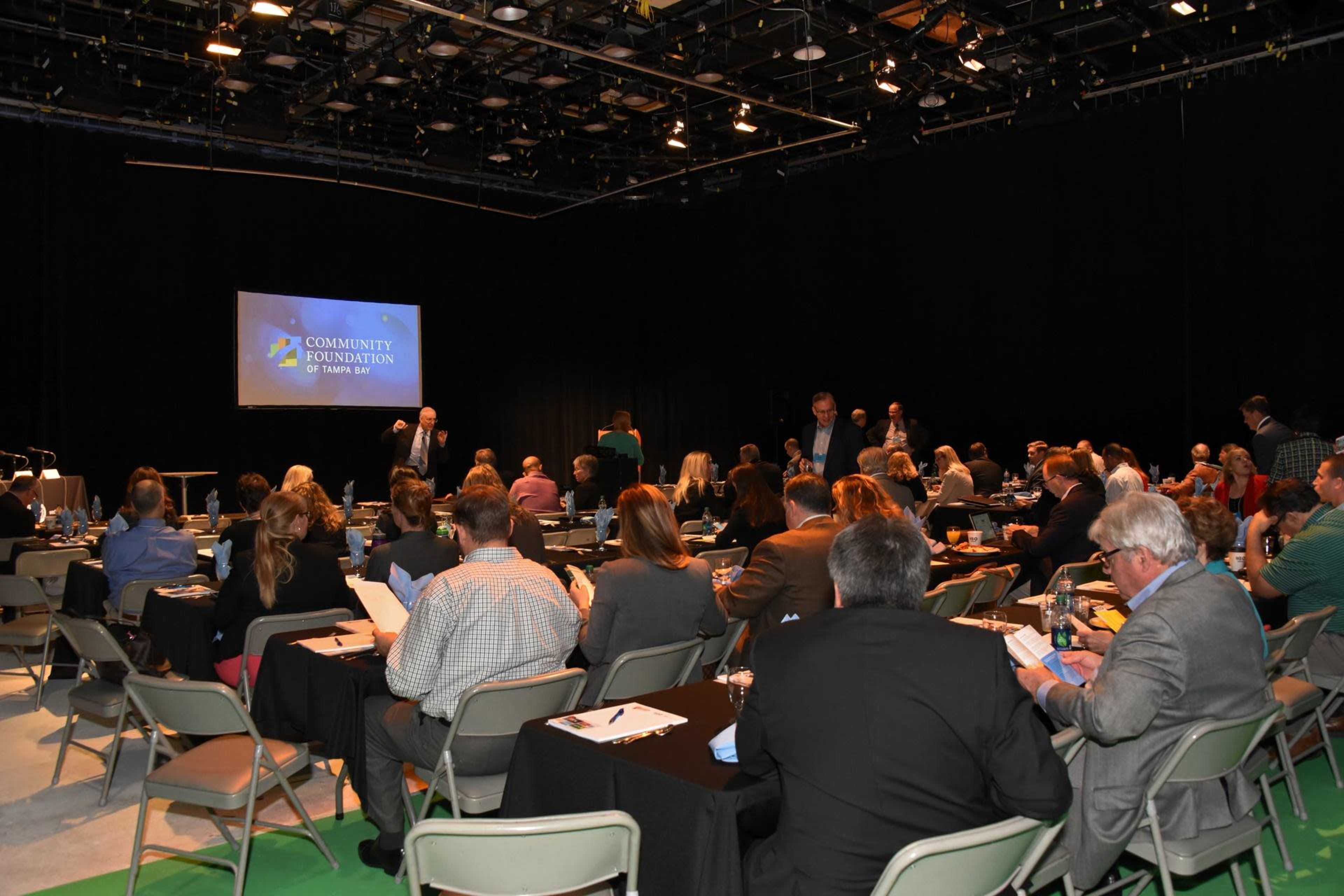 A group of people is seated in a conference room with tables, preparing for an event hosted by the Community Foundation.