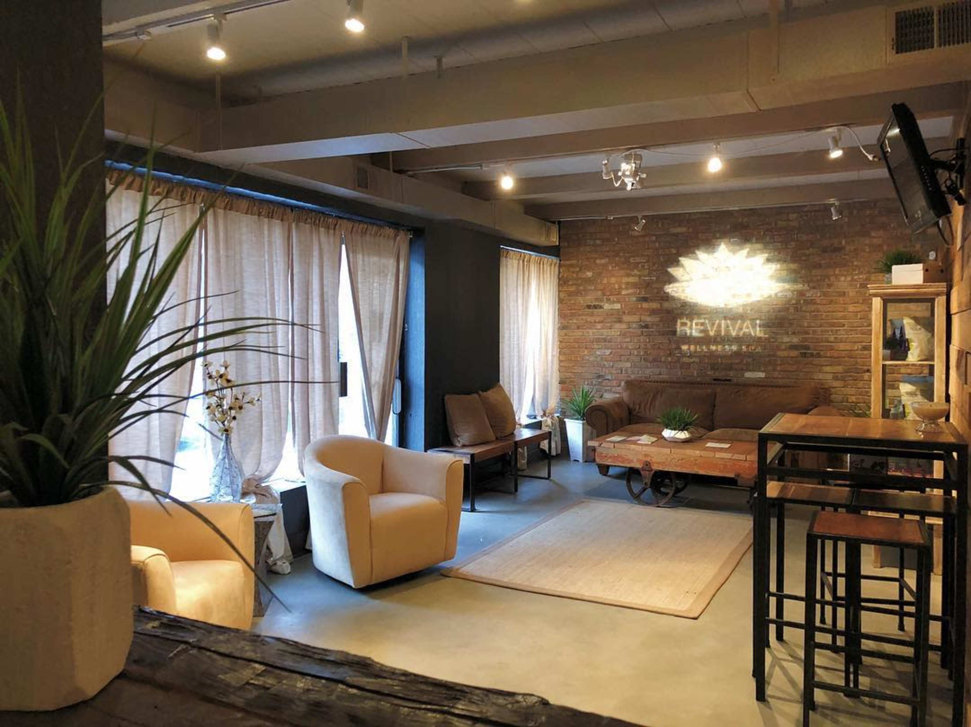 A cozy lounge area featuring brown leather chairs, a wooden coffee table, and a decorative wall with the word "REVIVAL" illuminated.