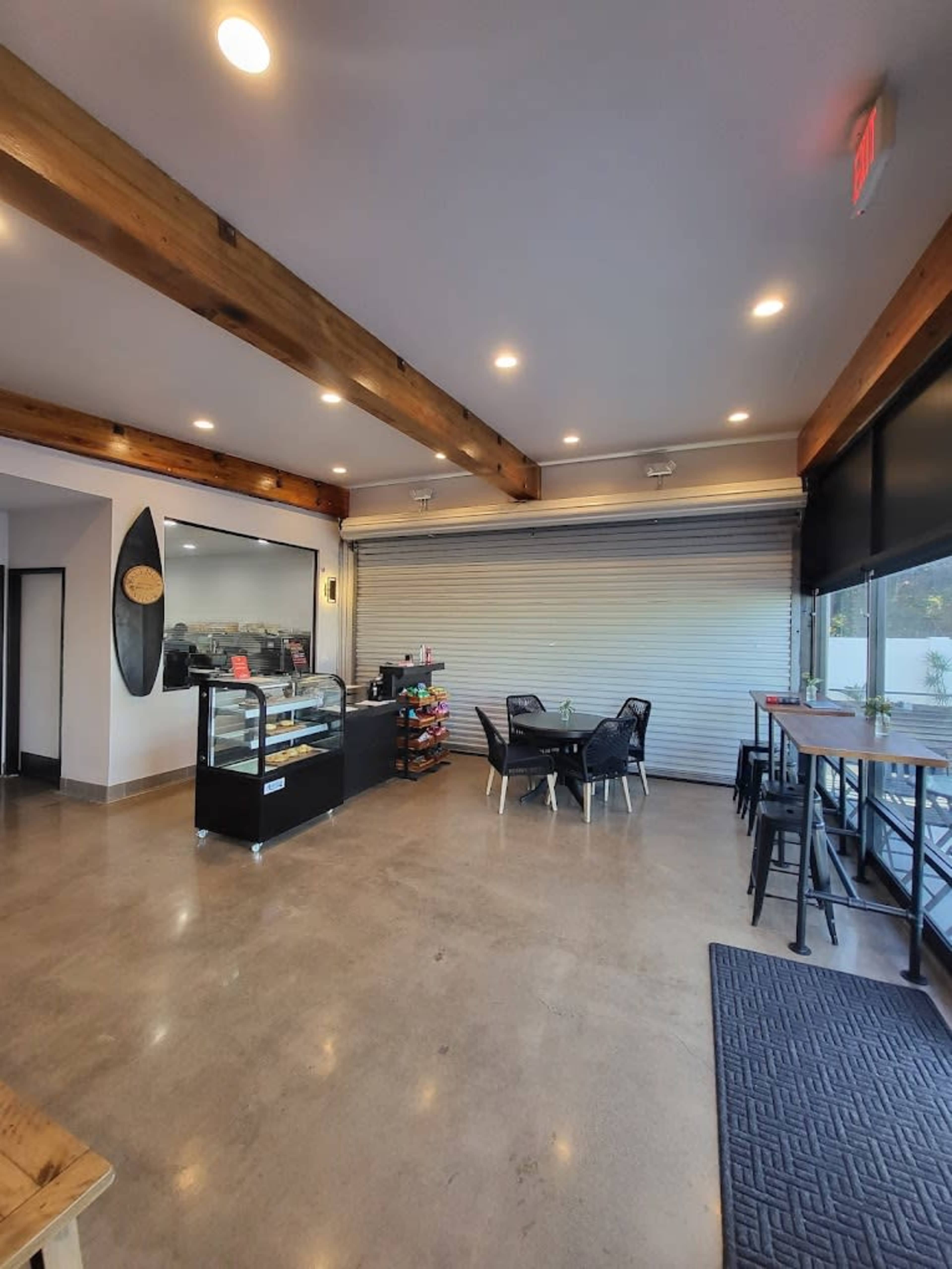 A modern café interior with wooden beams, an enclosed display case for pastries, and seating areas featuring black chairs and tables.