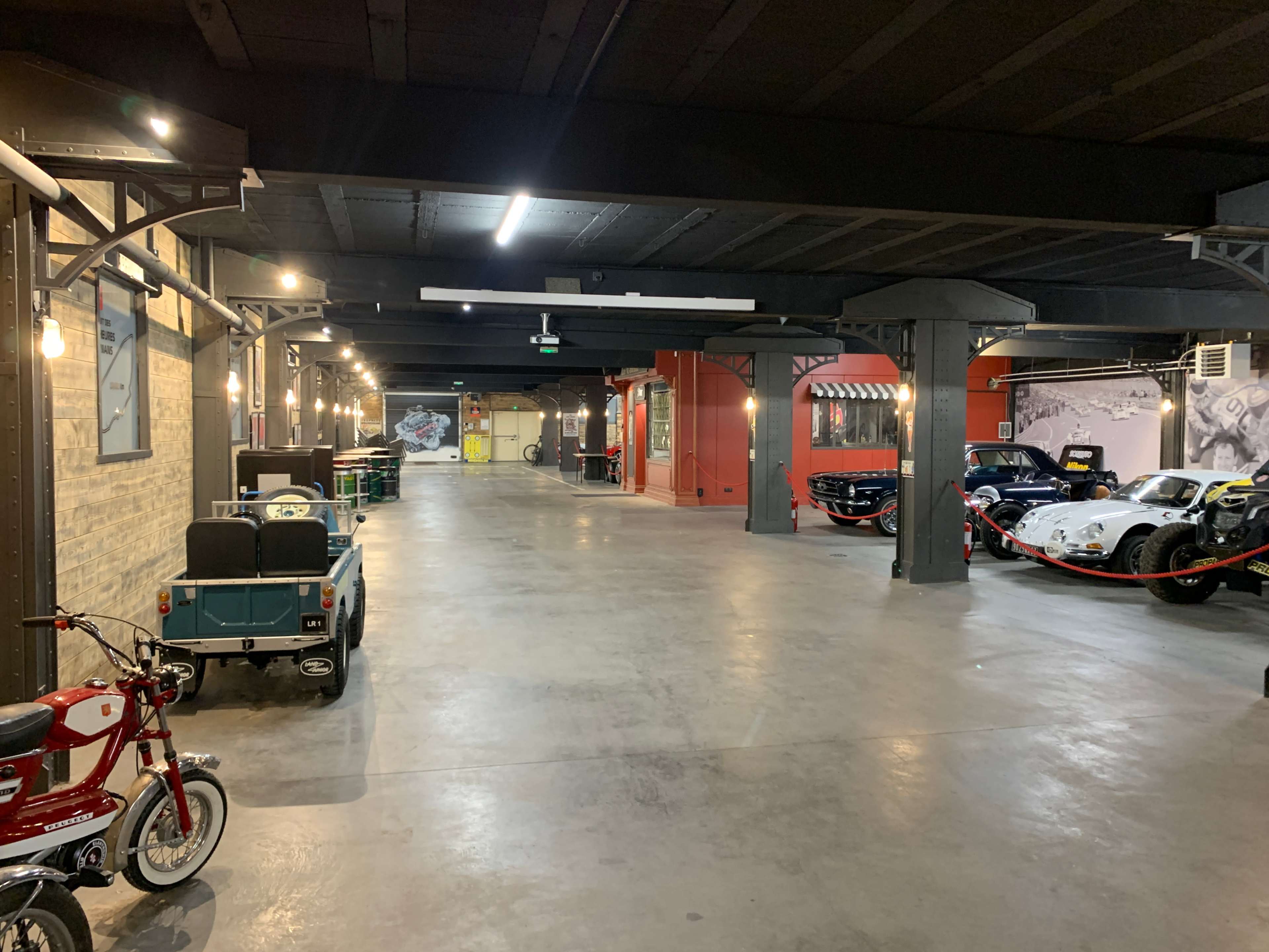 The image features an industrial-style garage with a spacious hallway, showcasing various vehicles and bright overhead lighting.