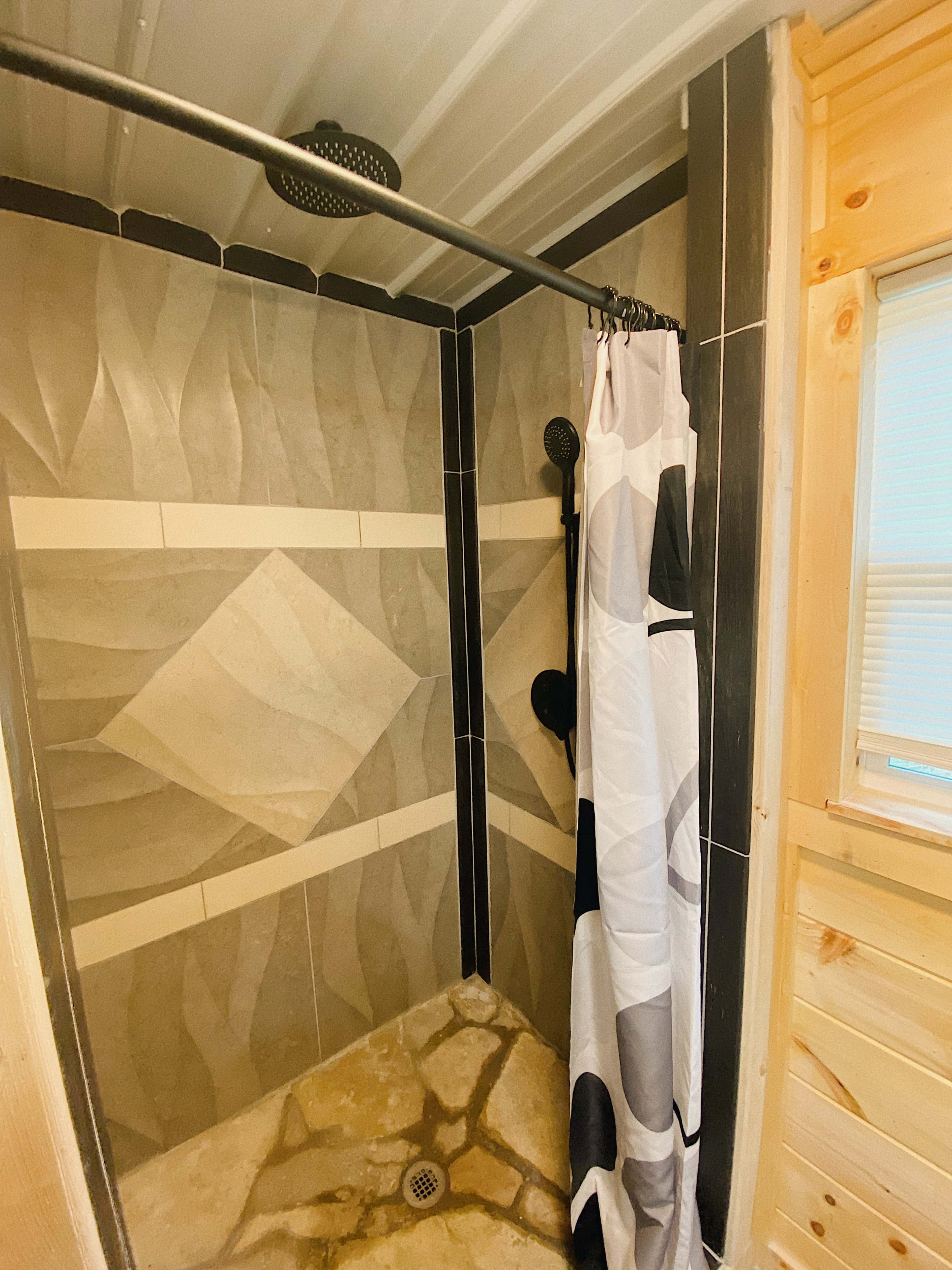 The image shows a shower area with patterned gray tiles, a shower curtain, and multiple showerheads.
