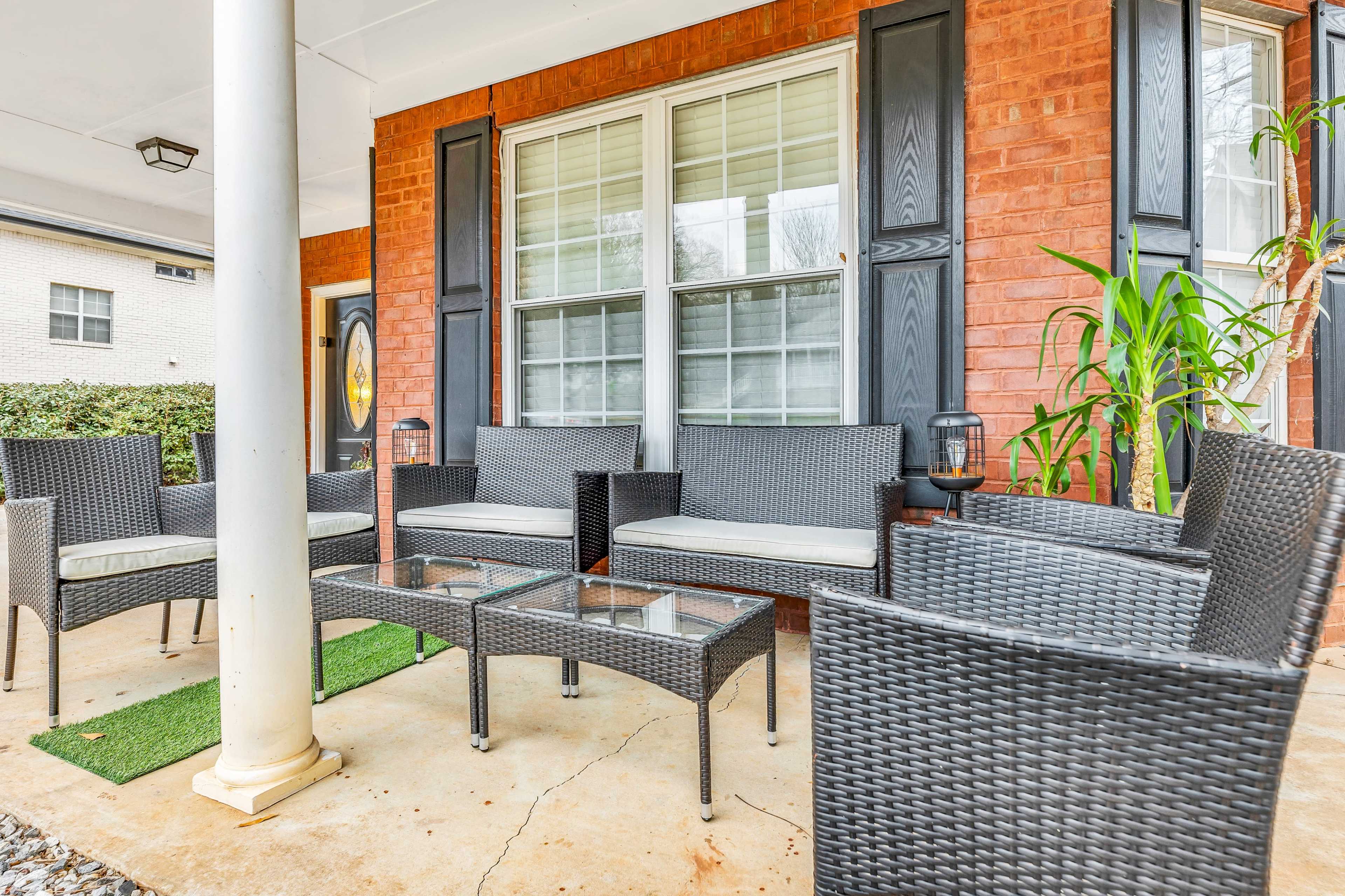 The image shows an outdoor seating area with woven furniture arranged around a glass coffee table on a covered porch.