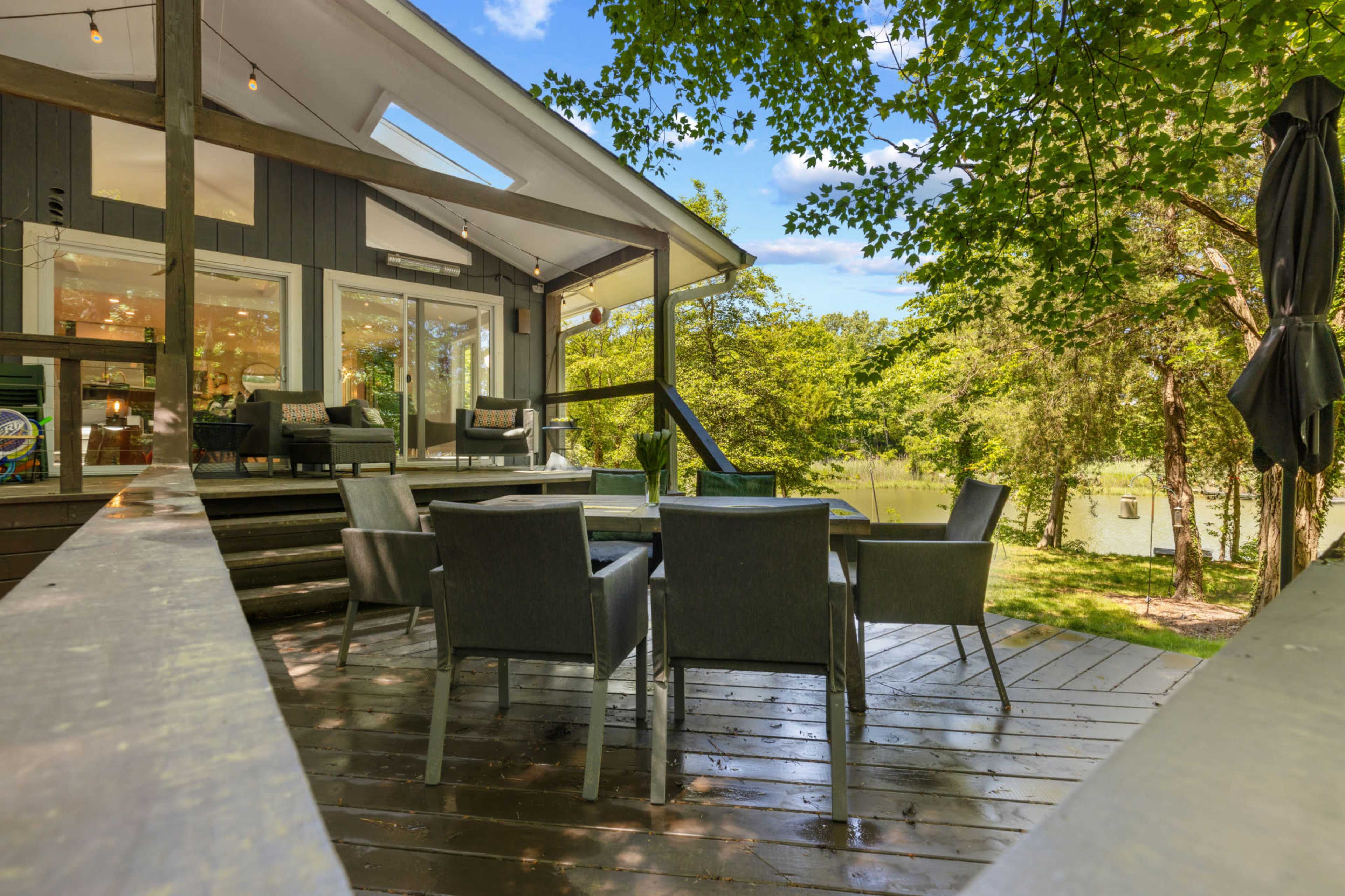 A wooden deck with outdoor seating overlooks a tranquil body of water, surrounded by trees.
