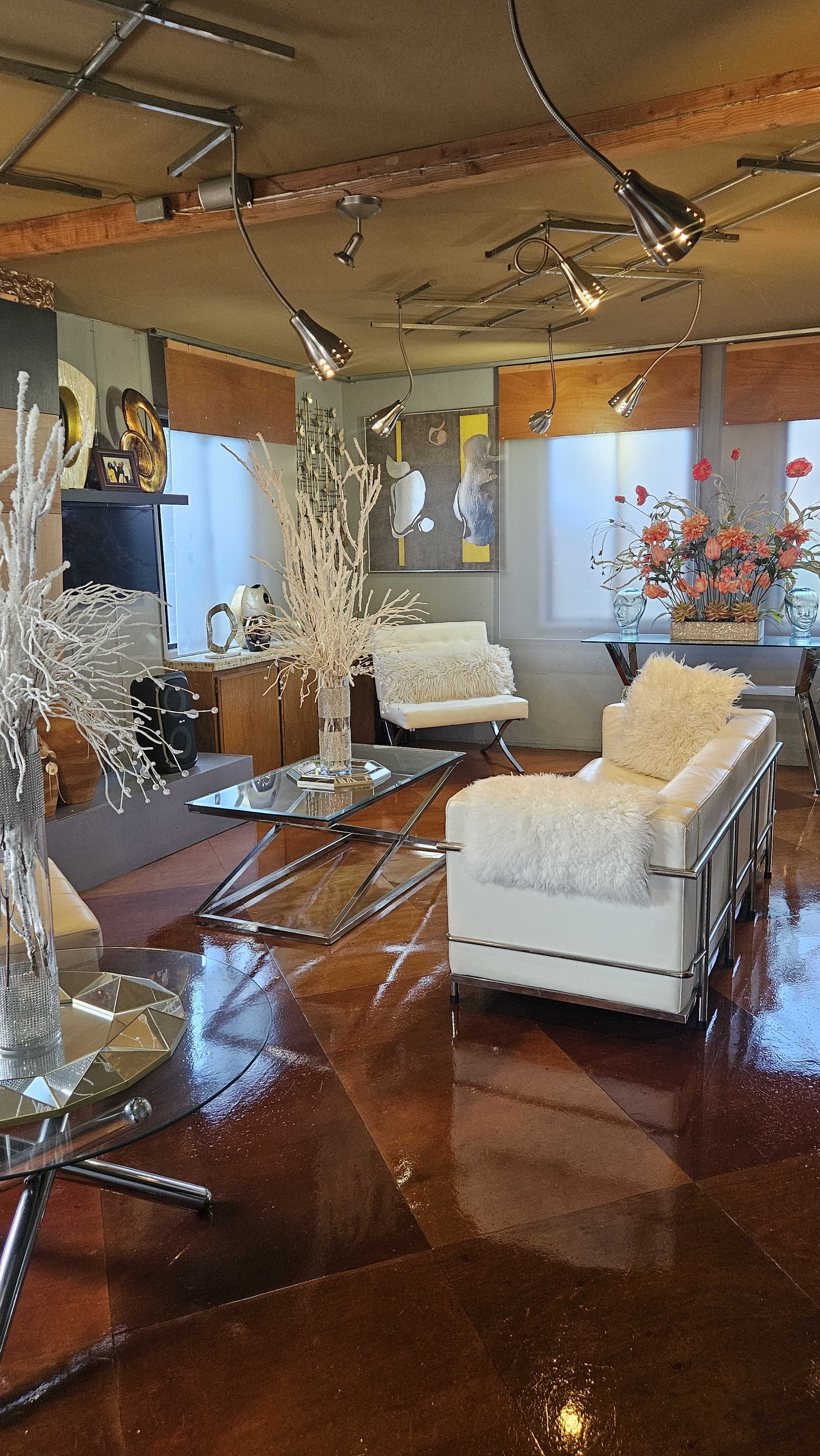 The image shows a modern living room with sleek white furniture, polished brown floors, and decorative elements such as vases and floral arrangements.