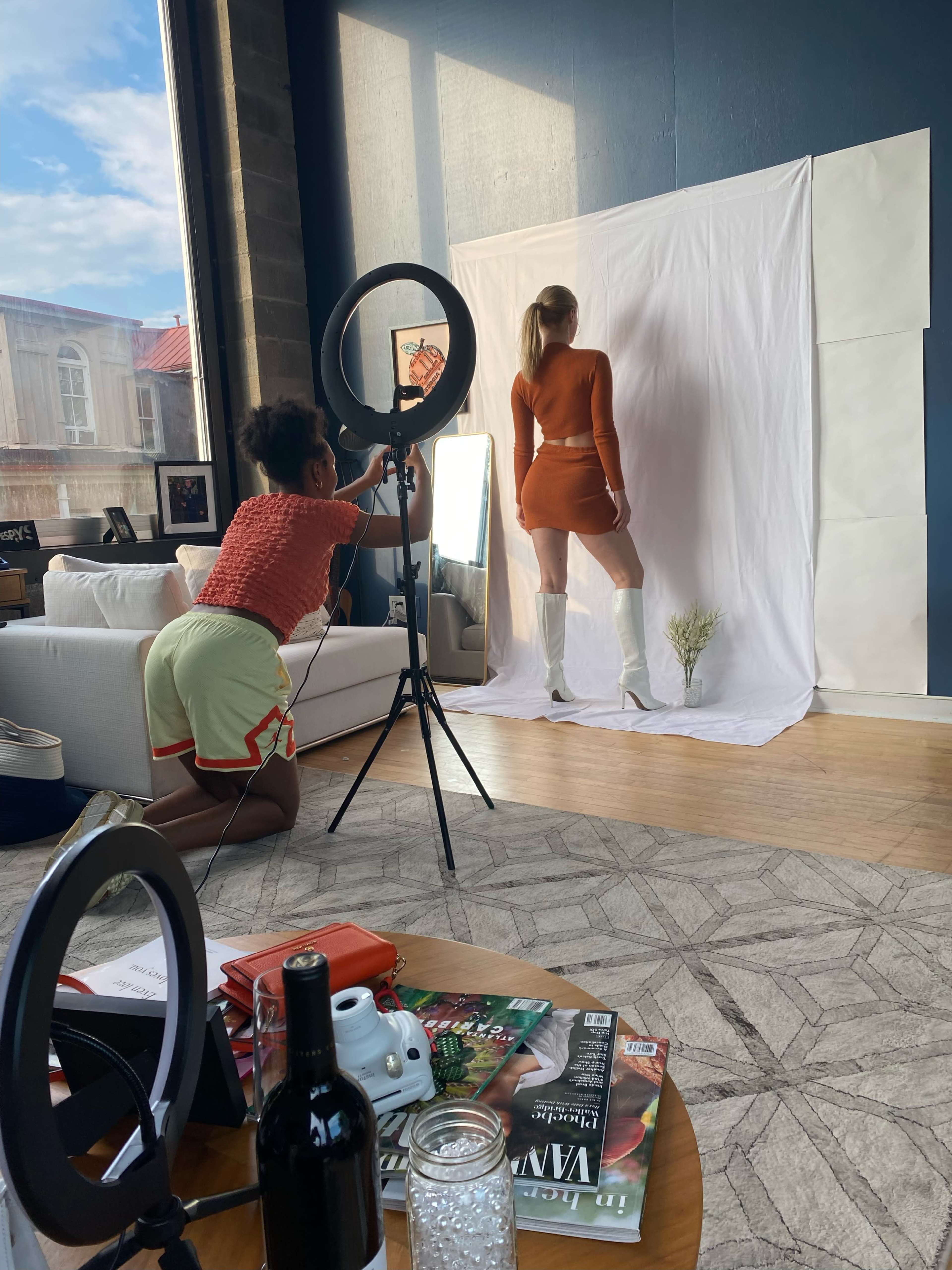 A photographer captures a model posed against a white backdrop in a well-lit studio.