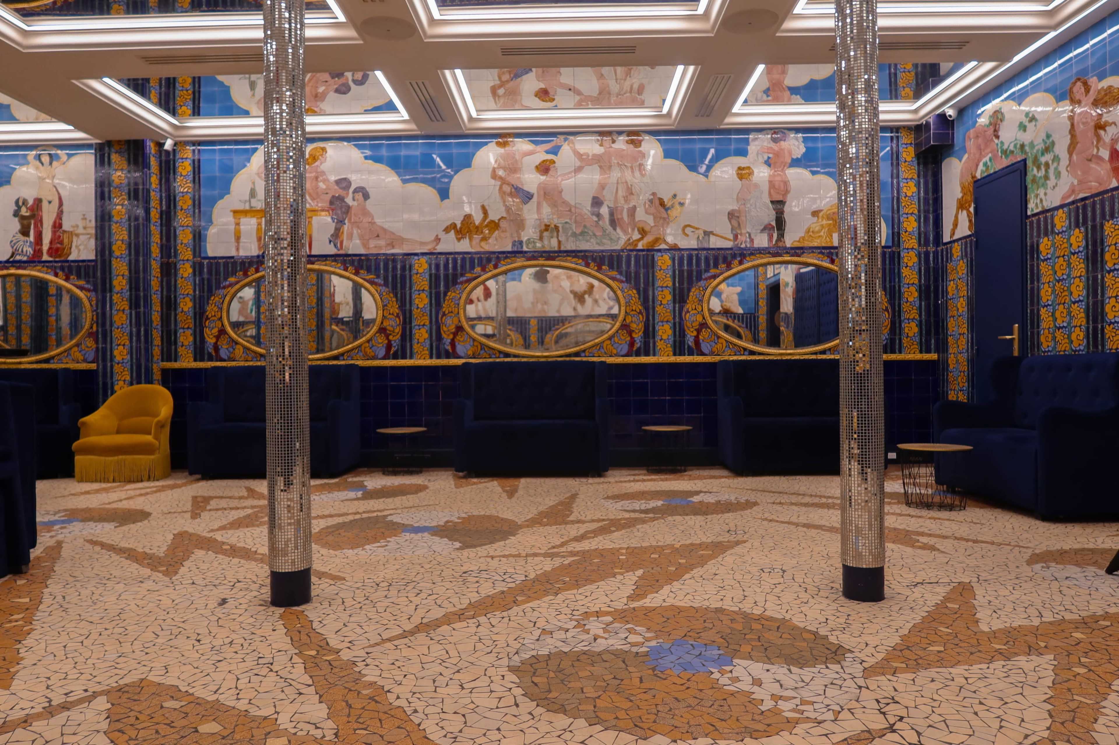 A colorful interior space featuring mosaic flooring, ornate wall murals, and plush seating arrangements.