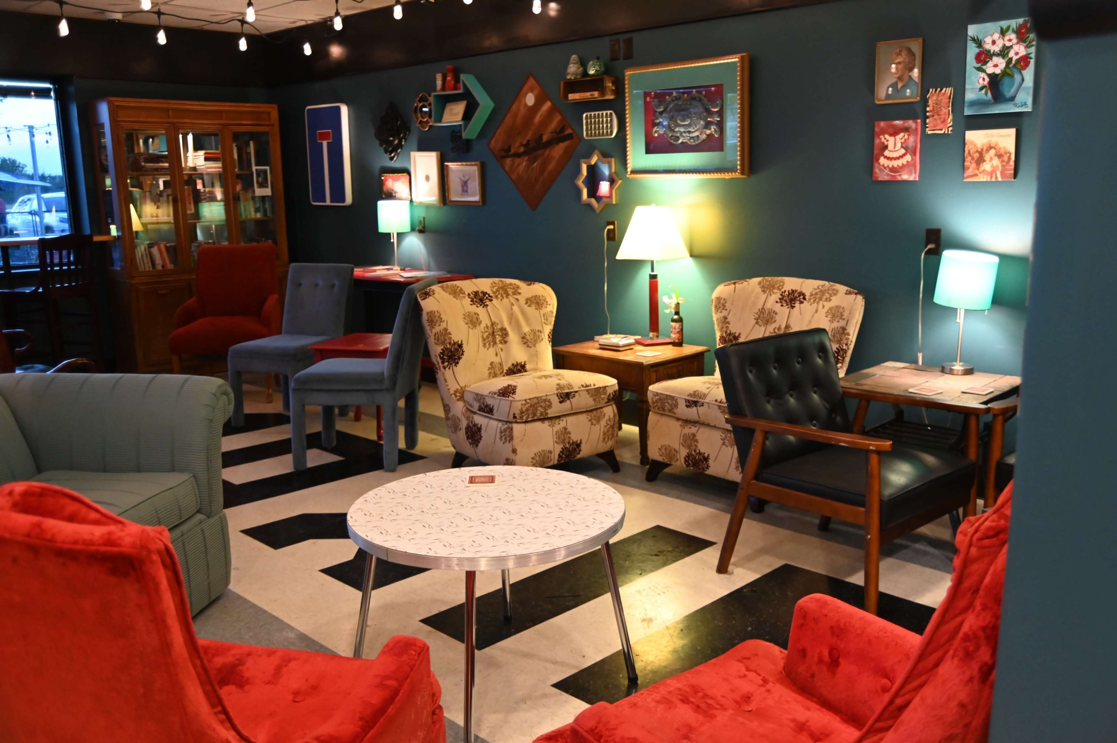 The image depicts a cozy lounge area with colorful chairs, a round table, and various artwork on the walls, all arranged on a black and white checkered floor.