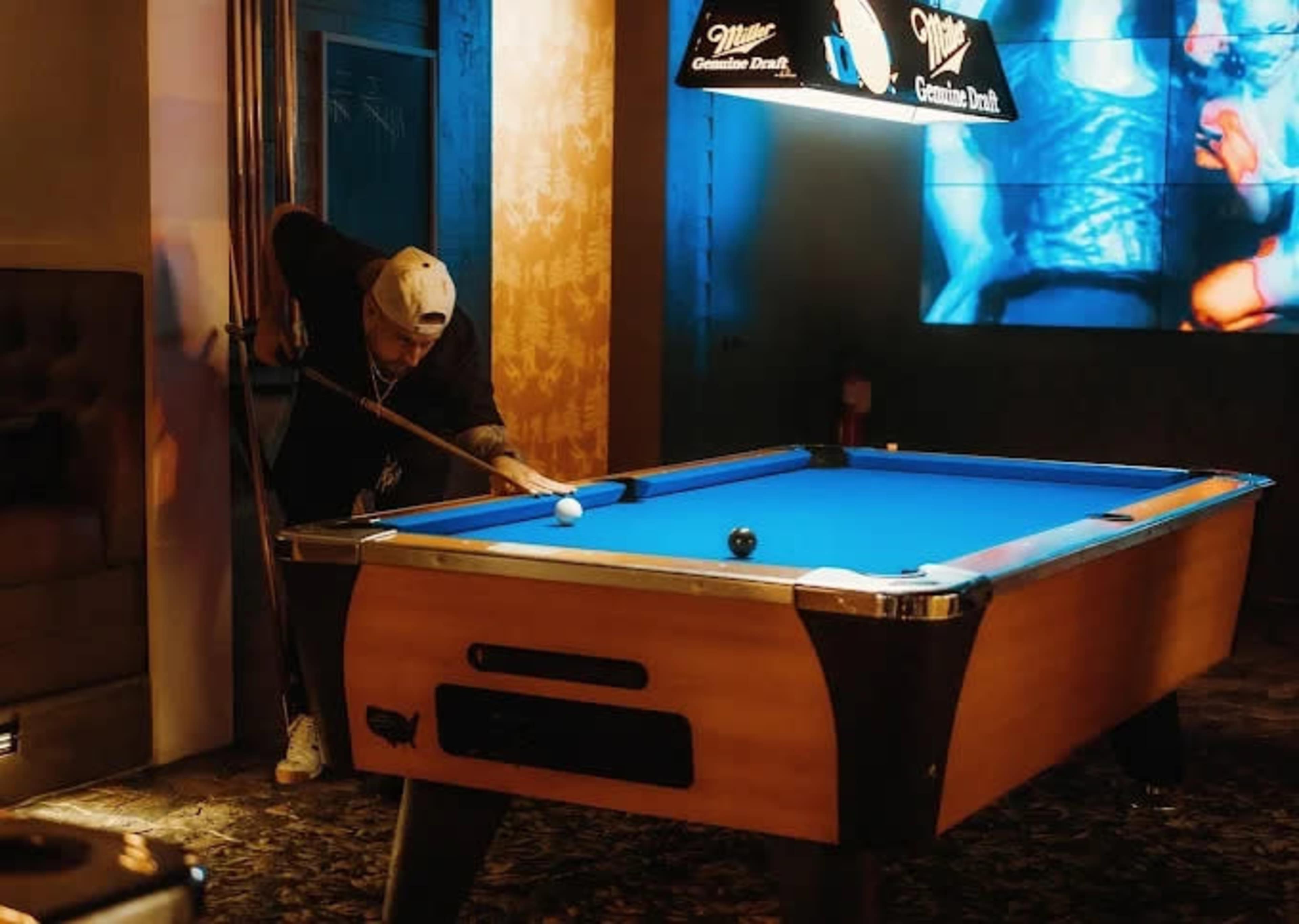 A person stands at a pool table, preparing to take a shot in a dimly lit bar.