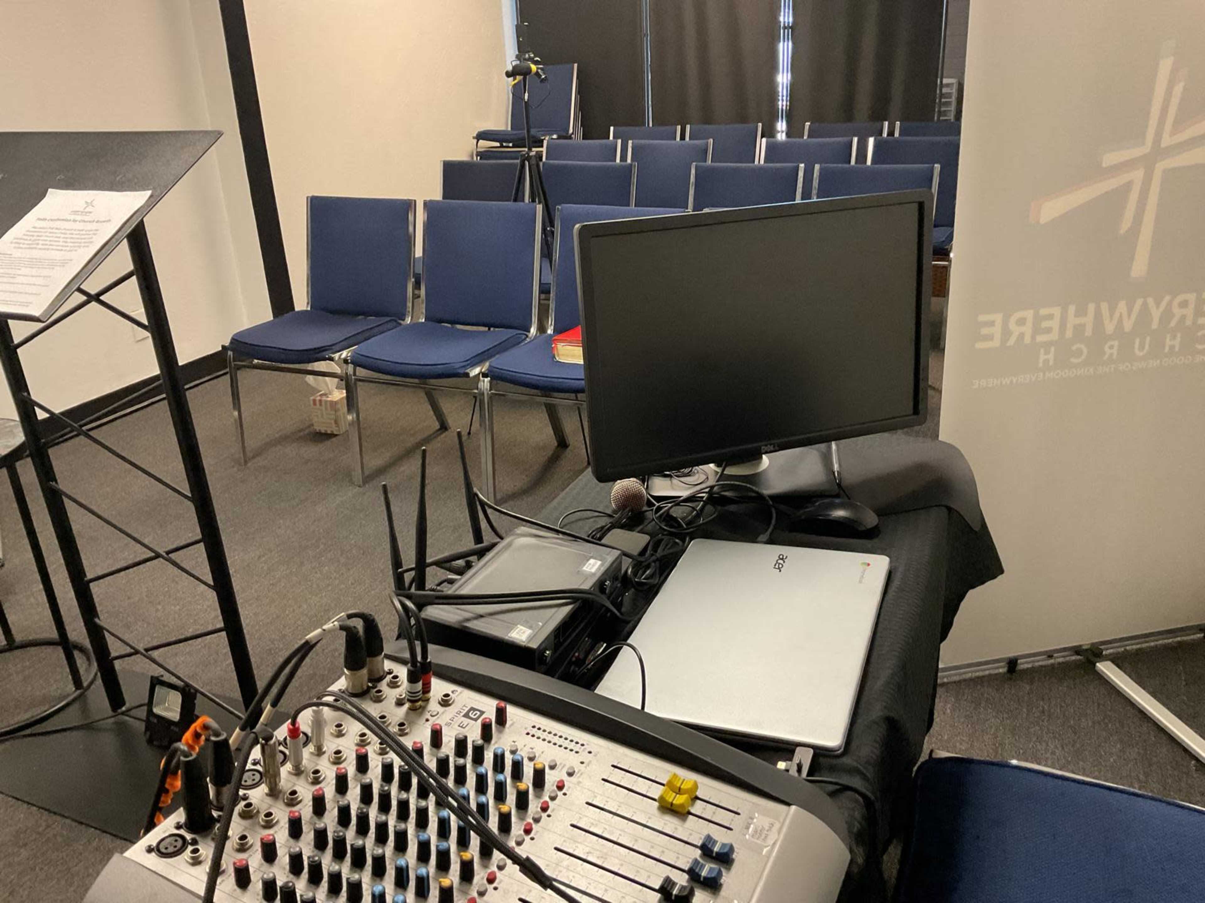 A sound mixing board and a computer are set up in front of empty chairs arranged for an event or presentation in a conference room.