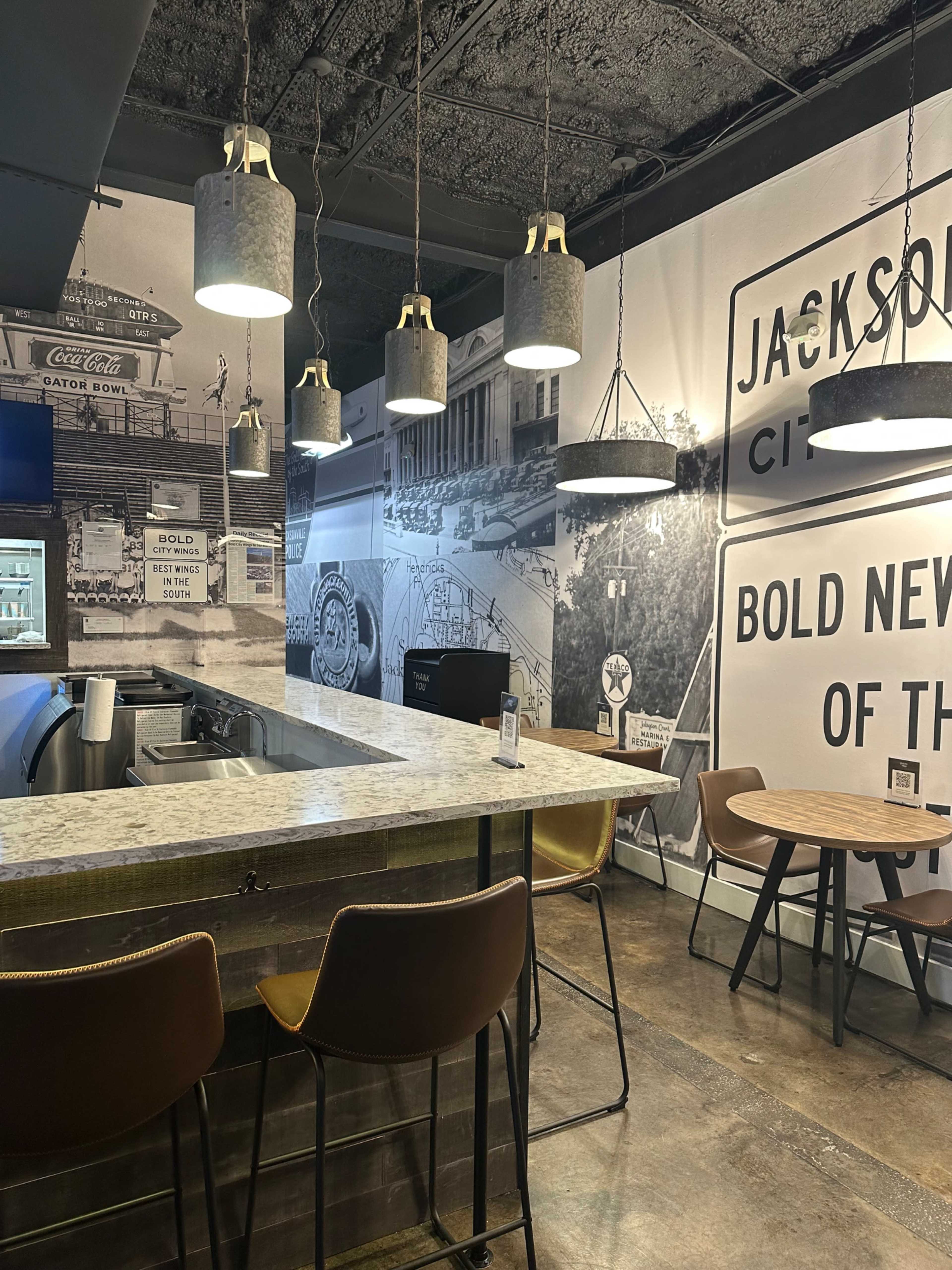 The image shows a modern café interior featuring a bar counter with a granite top, wooden stools, and walls adorned with black and white historical photographs of Jackson City.
