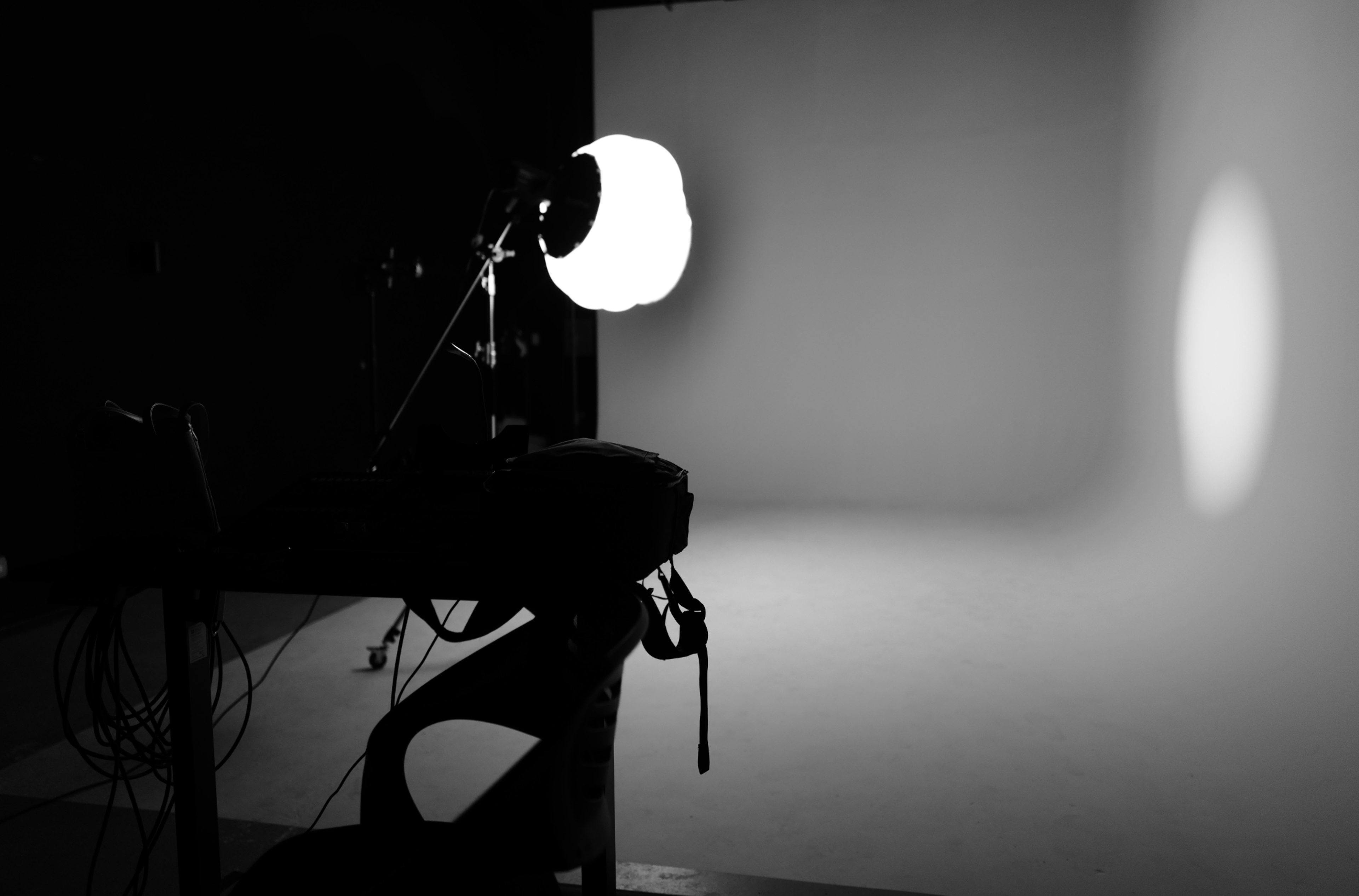 A photography studio is illuminated by a large softbox light, with a clear backdrop and equipment on a table in the foreground.