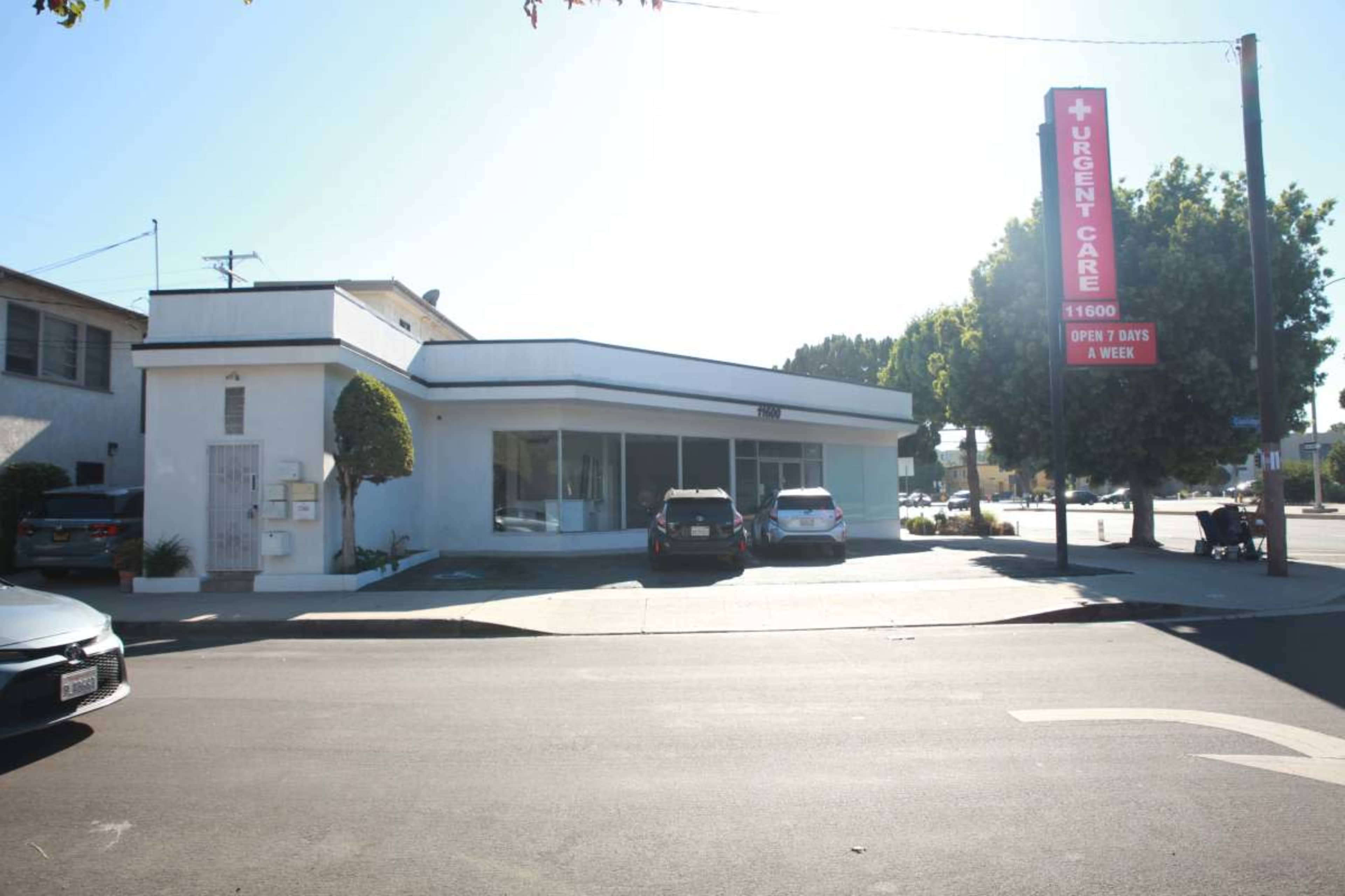 A single-story medical facility marked as "Urgent Care," featuring a large sign, situated on a street corner with several parked cars nearby.