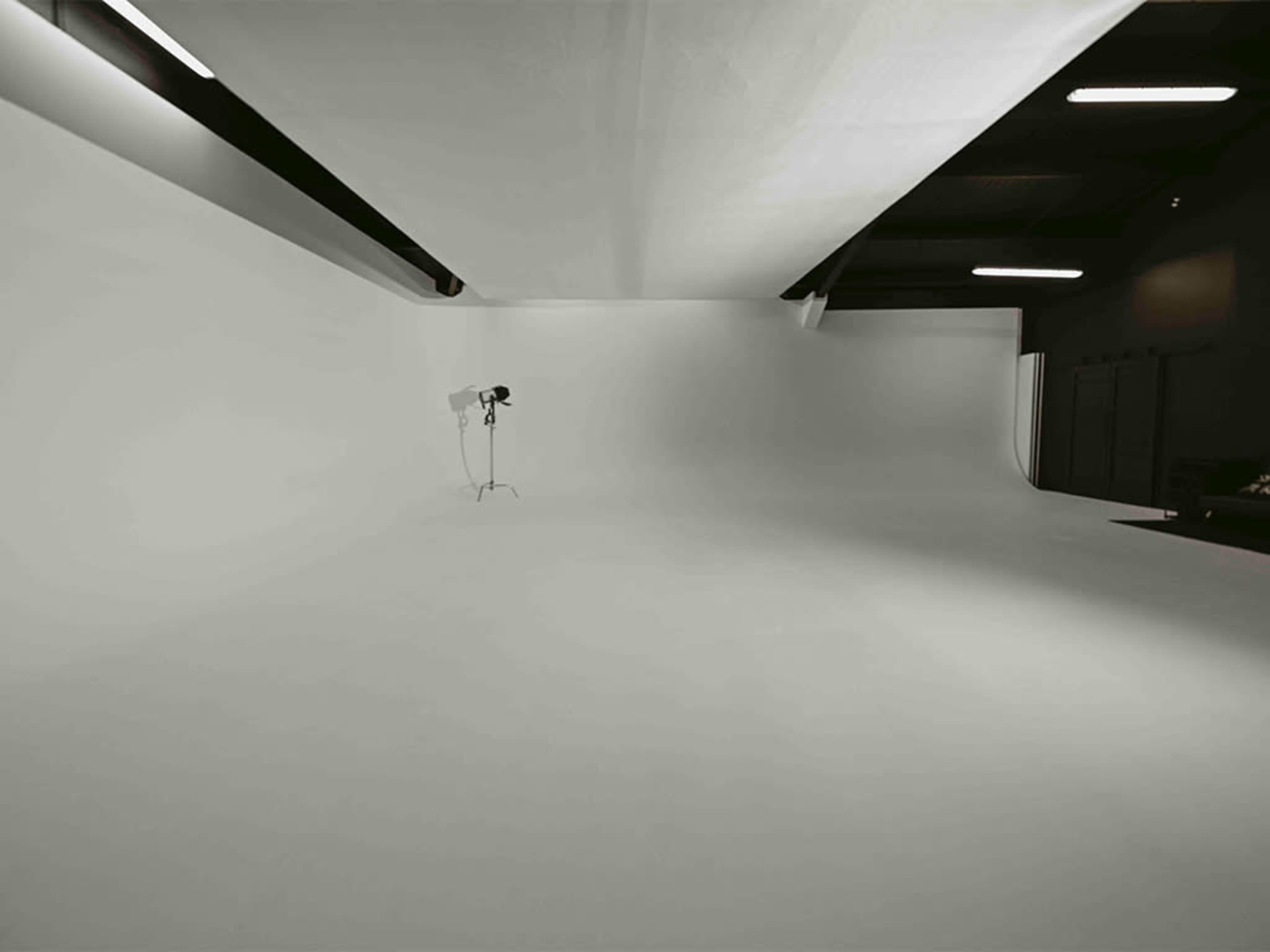 A spacious photography studio with a seamless white backdrop and a single light stand.