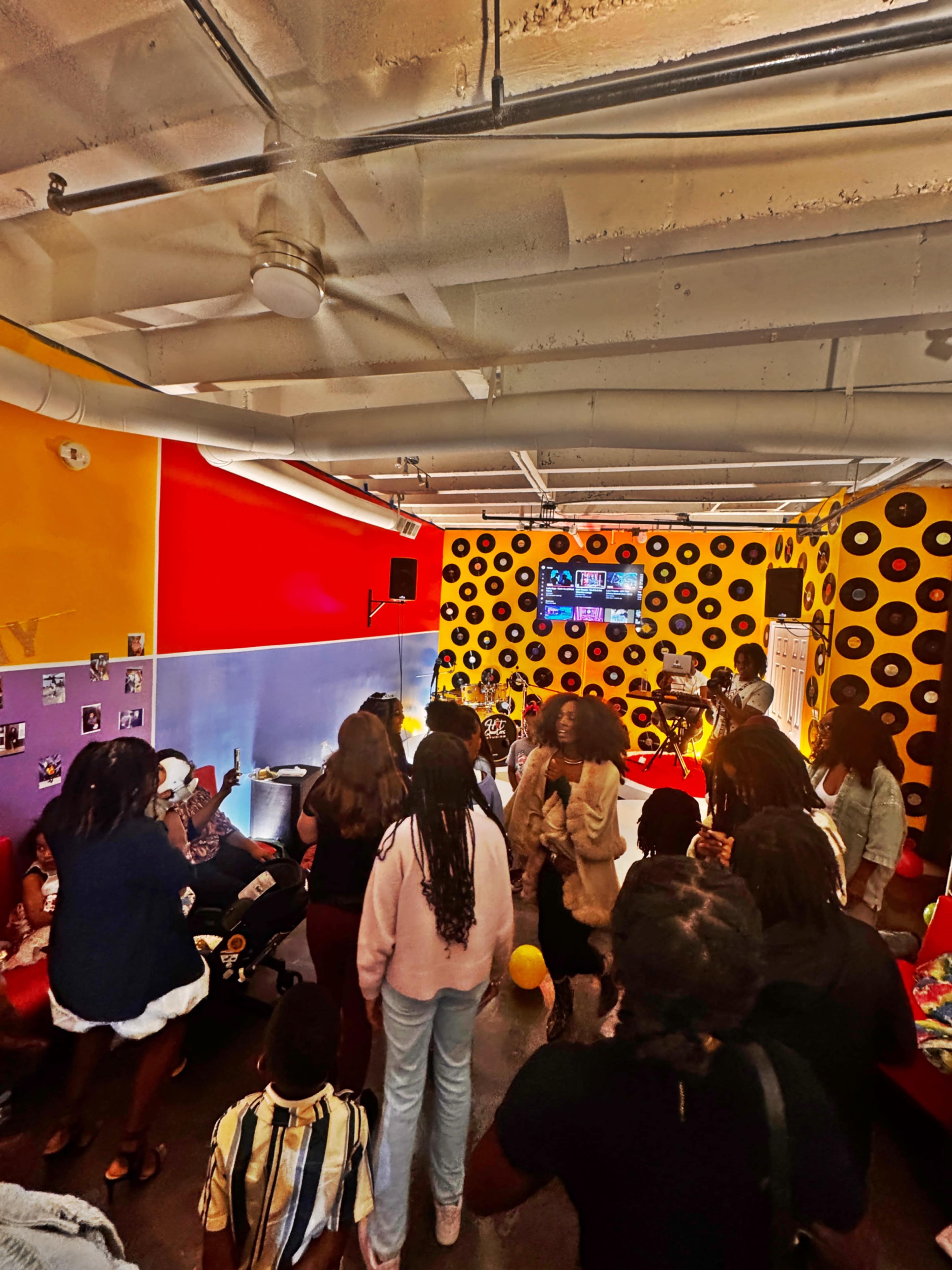 A lively gathering of people is taking place in a brightly decorated room featuring colorful walls and vinyl records.
