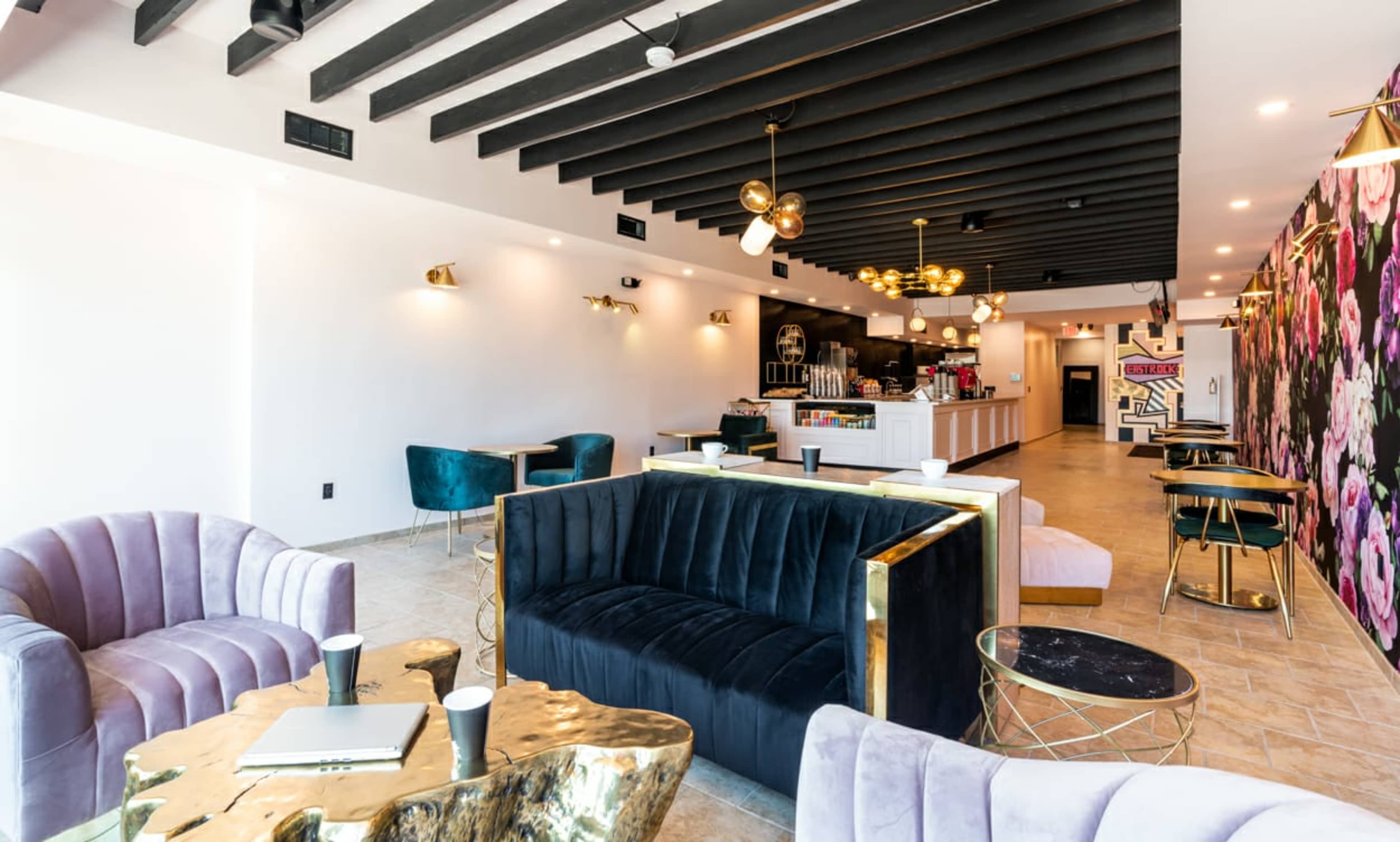 A modern café interior featuring a mix of plush seating, decorative light fixtures, and a floral accent wall.