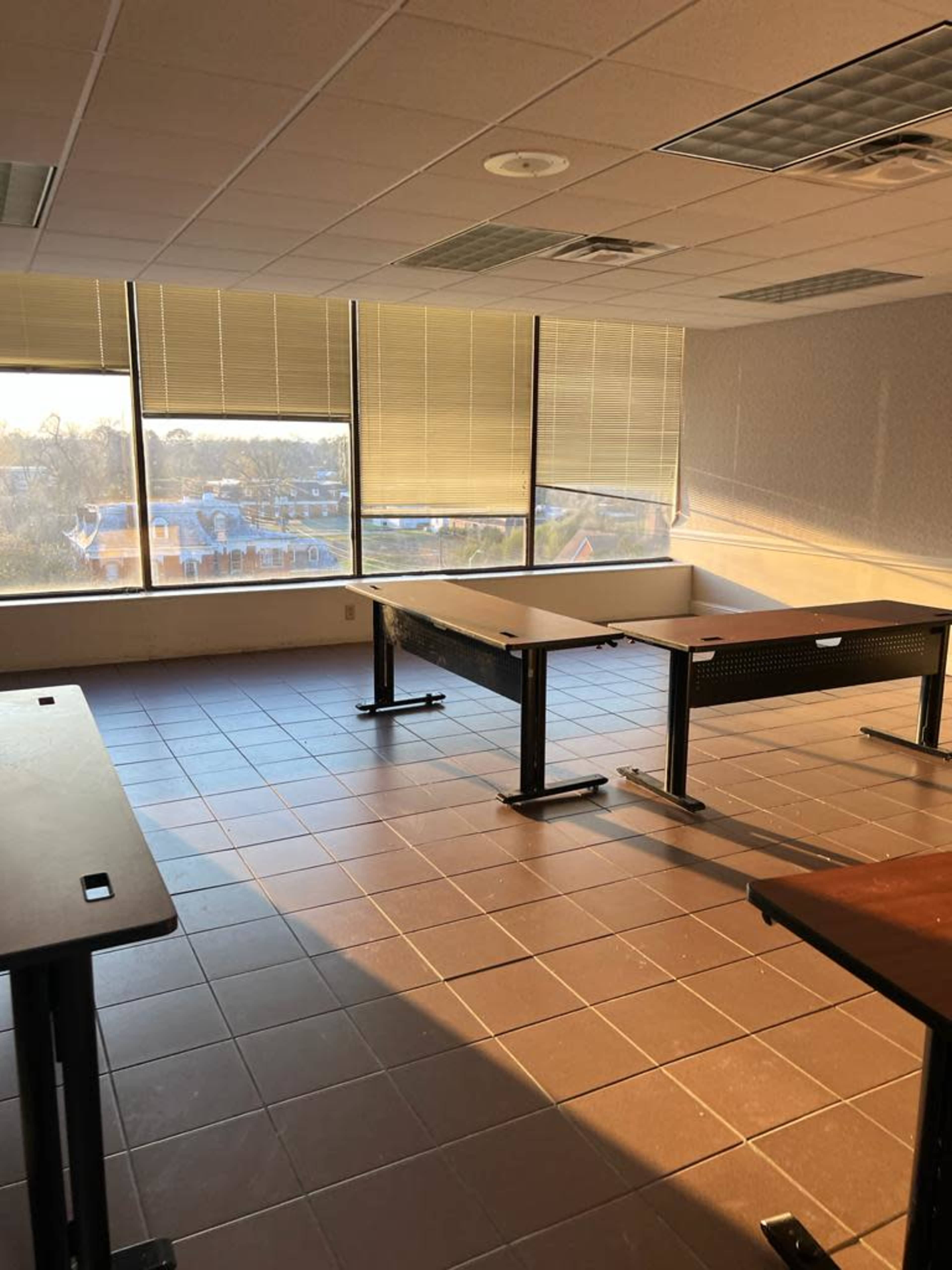 An empty classroom with large windows letting in natural light, featuring several tables arranged in the space.