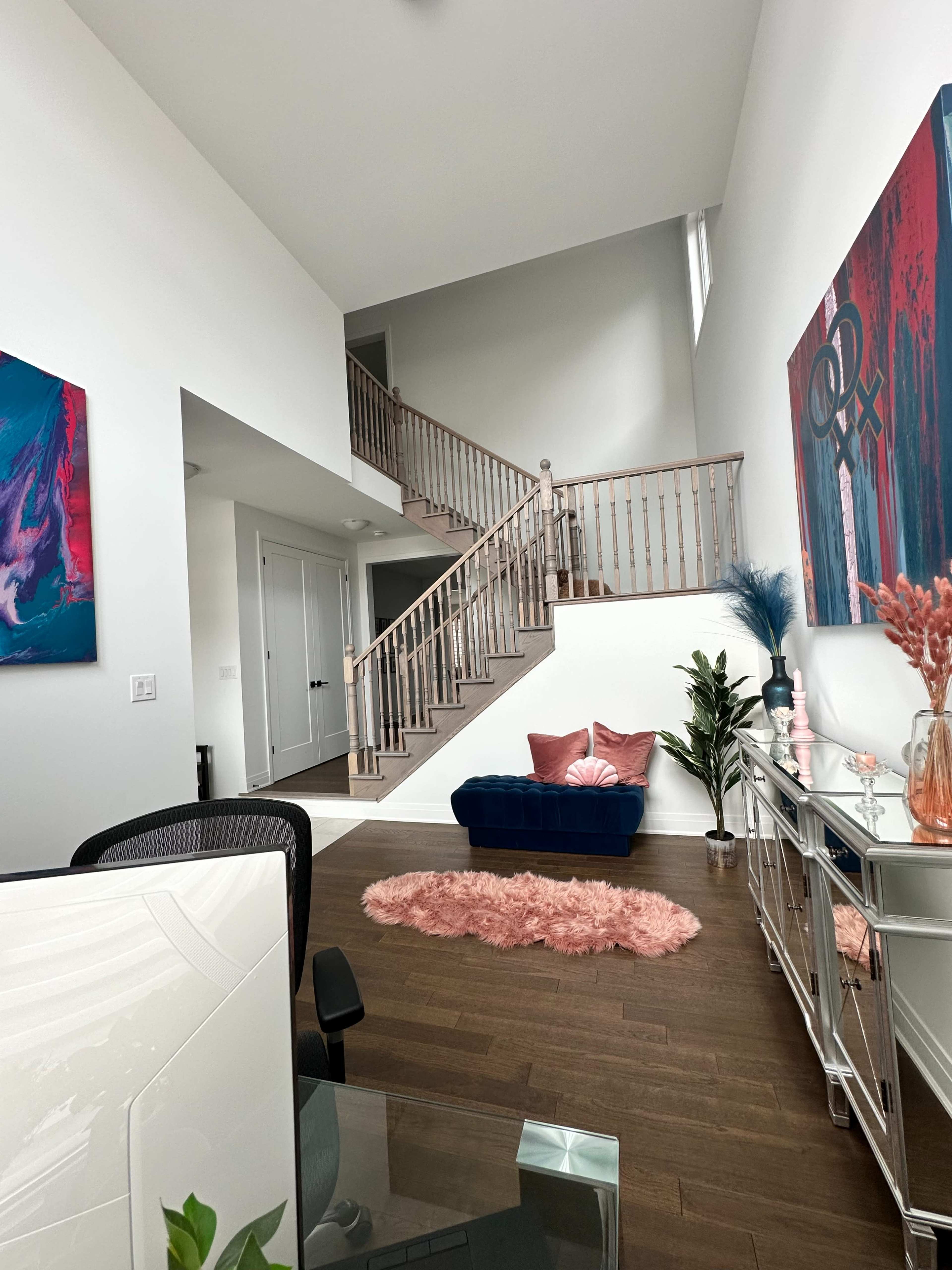 A bright, modern living space featuring a staircase, a blue couch, decorative plants, and colorful wall art.