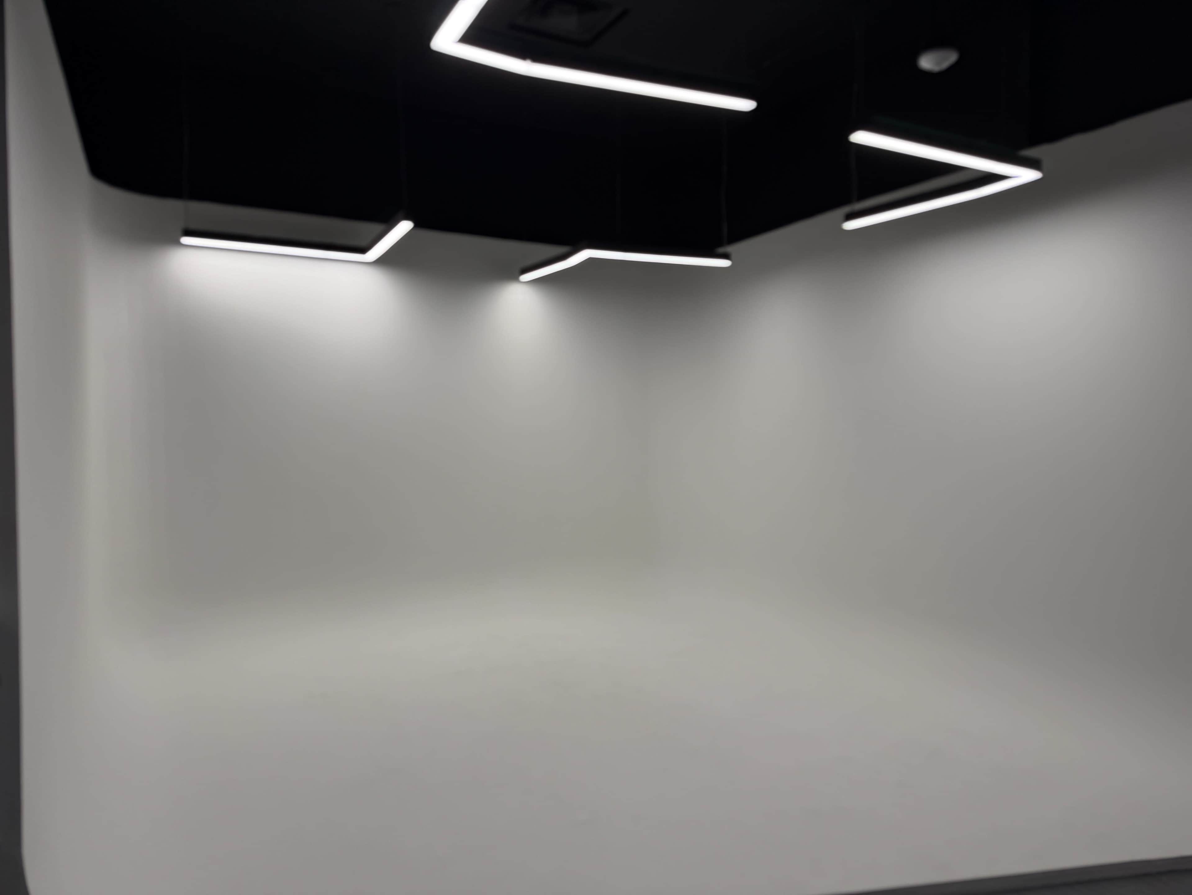 The image shows an empty room with a white walls and ceiling illuminated by modern rectangular light fixtures.