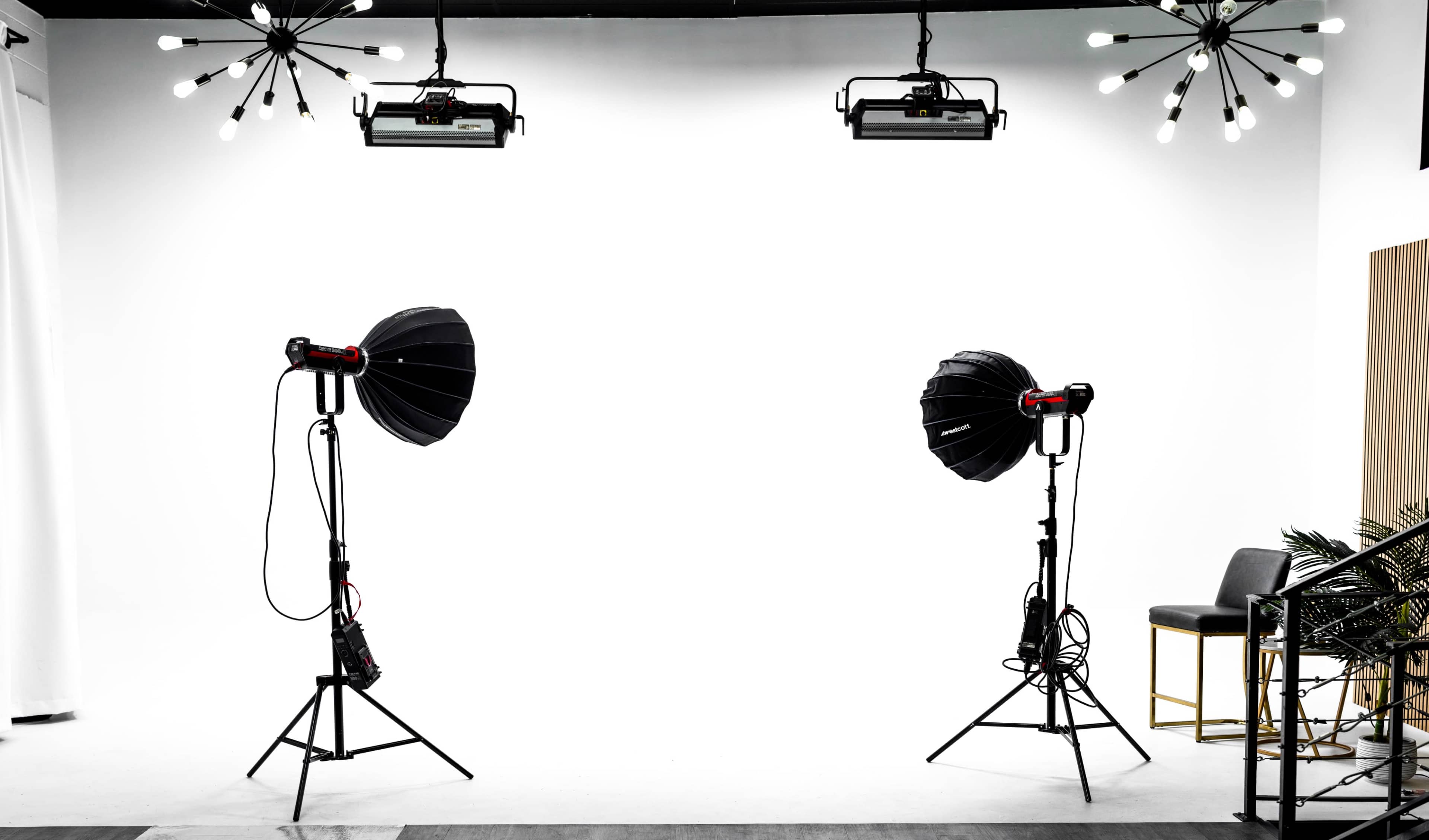 A photography studio with two large light fixtures on stands facing a blank white backdrop.