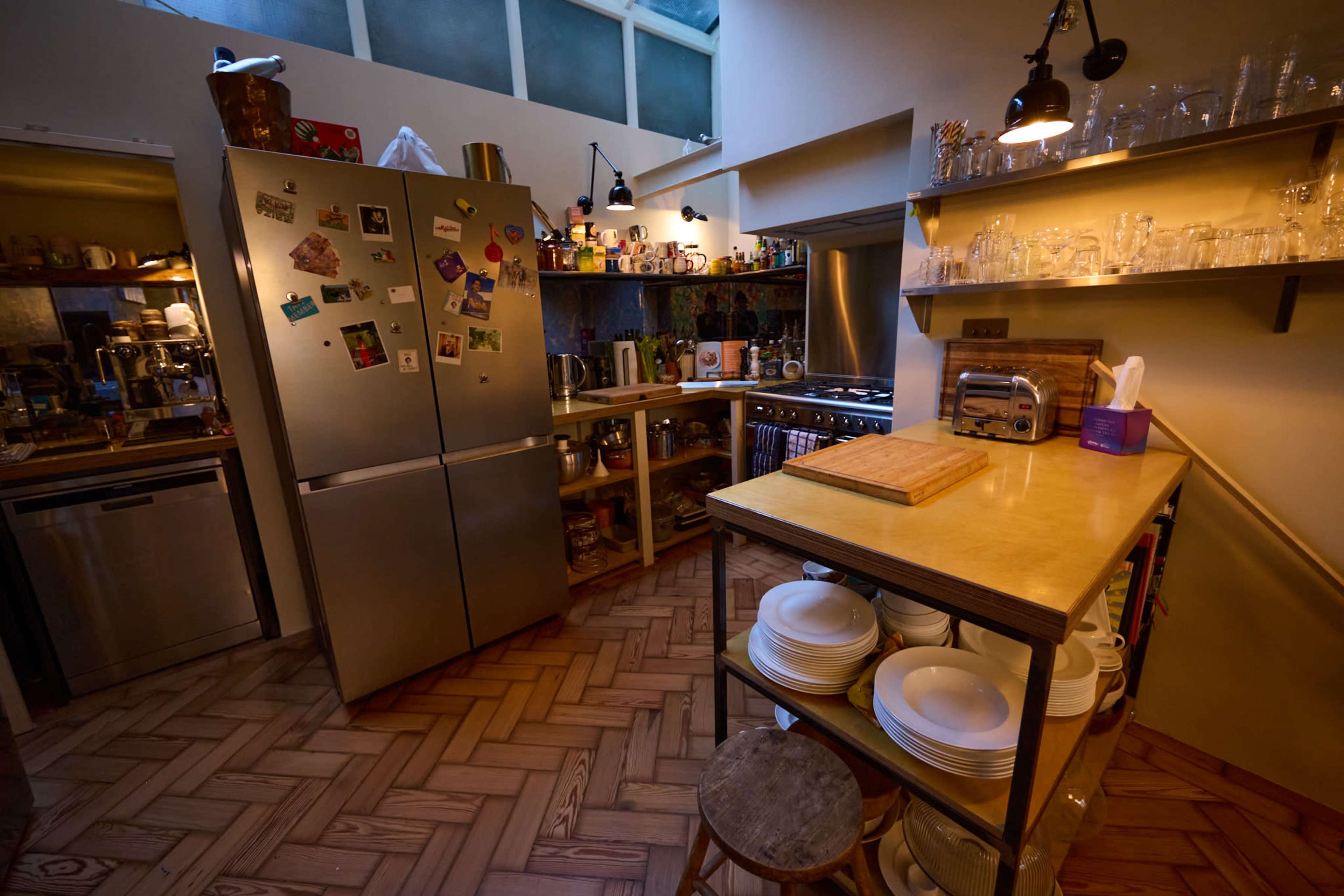 The image shows a well-organized kitchen featuring stainless steel appliances, a wooden countertop, and shelves stocked with glassware and utensils.
