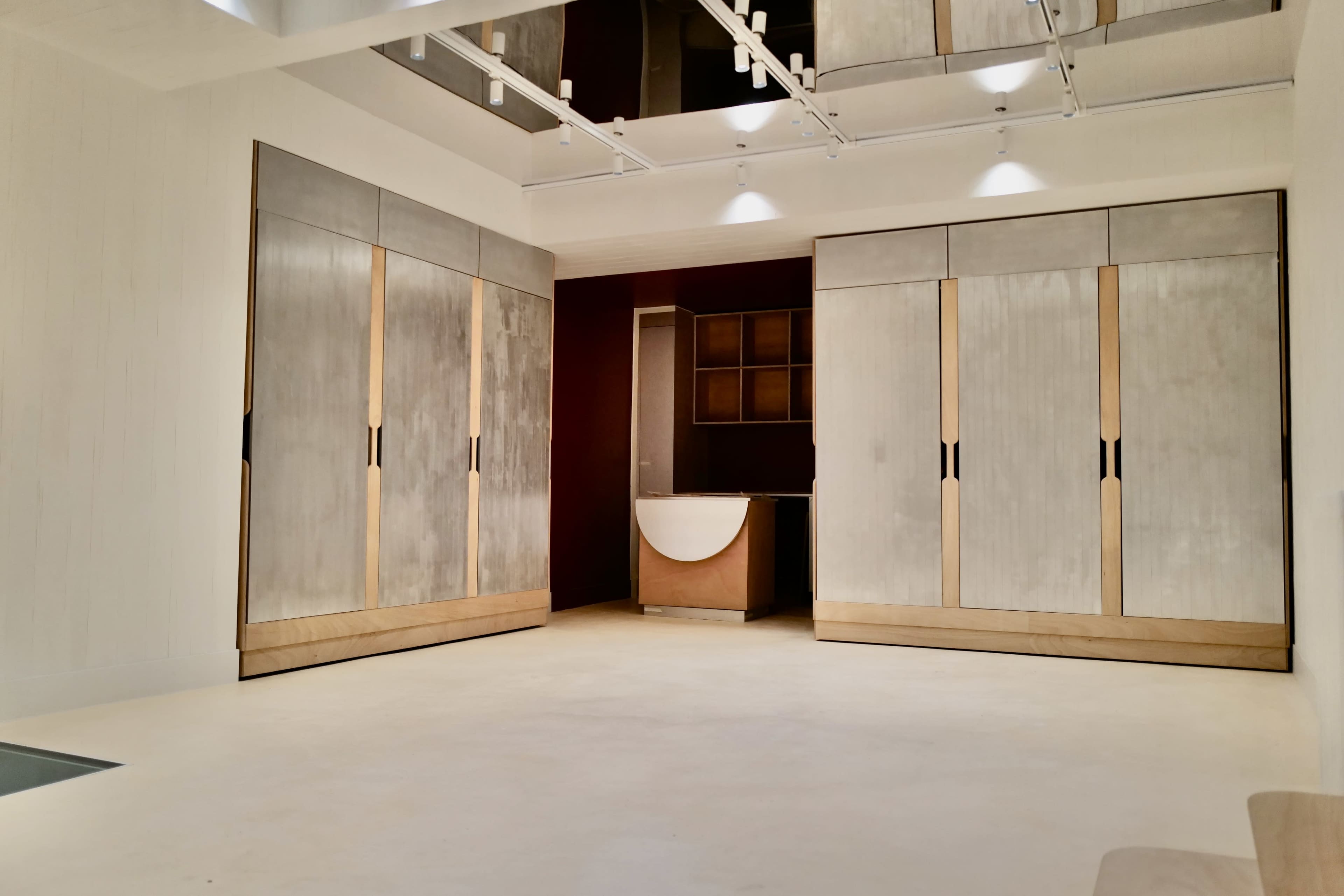 The image shows a spacious, modern interior featuring large cabinets, a minimalist reception area, and reflective ceilings.