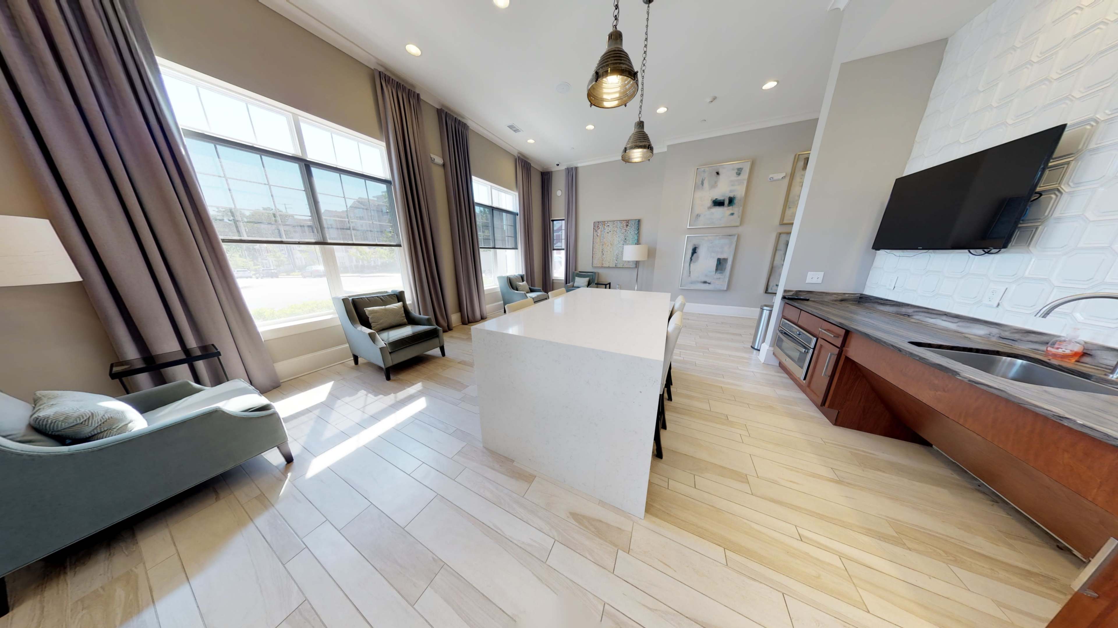 A modern interior space with a light-colored kitchen island, gray seating, large windows, and hardwood flooring.