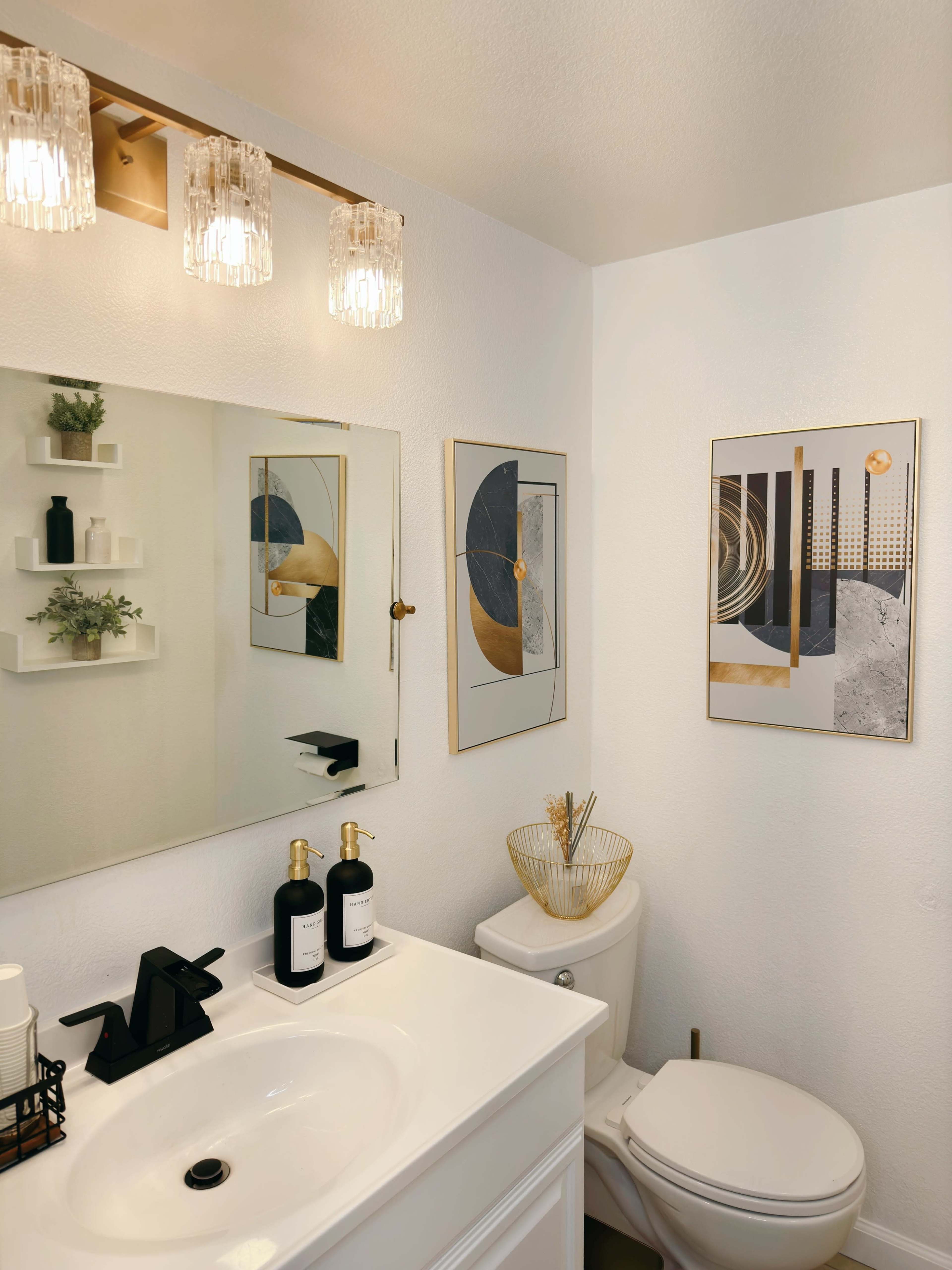 A modern bathroom features a white vanity with a sink, wall-mounted mirror, decorative art pieces, and sleek fixtures.