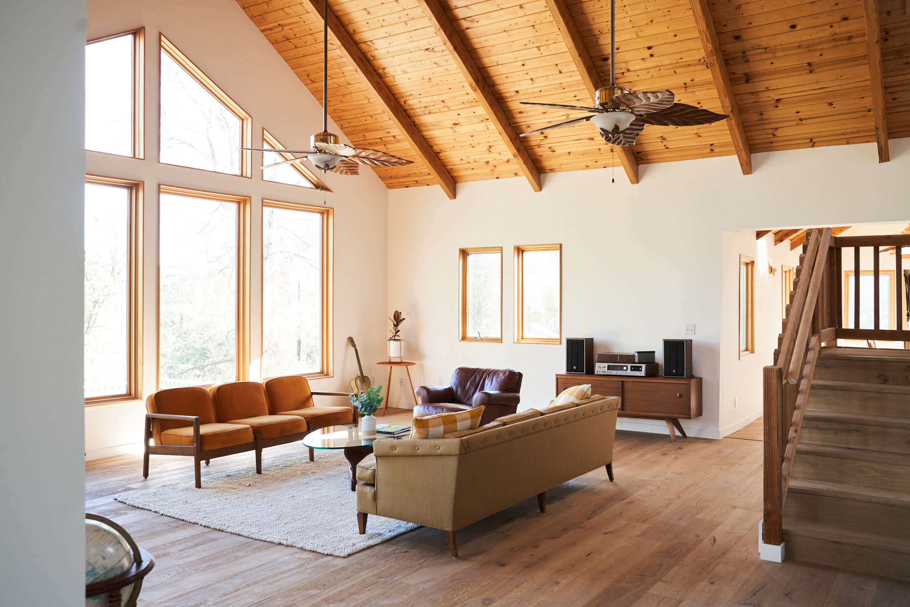 A spacious living room with large windows, wooden beams, and a mix of seating including a brown leather chair and a yellow sofa.