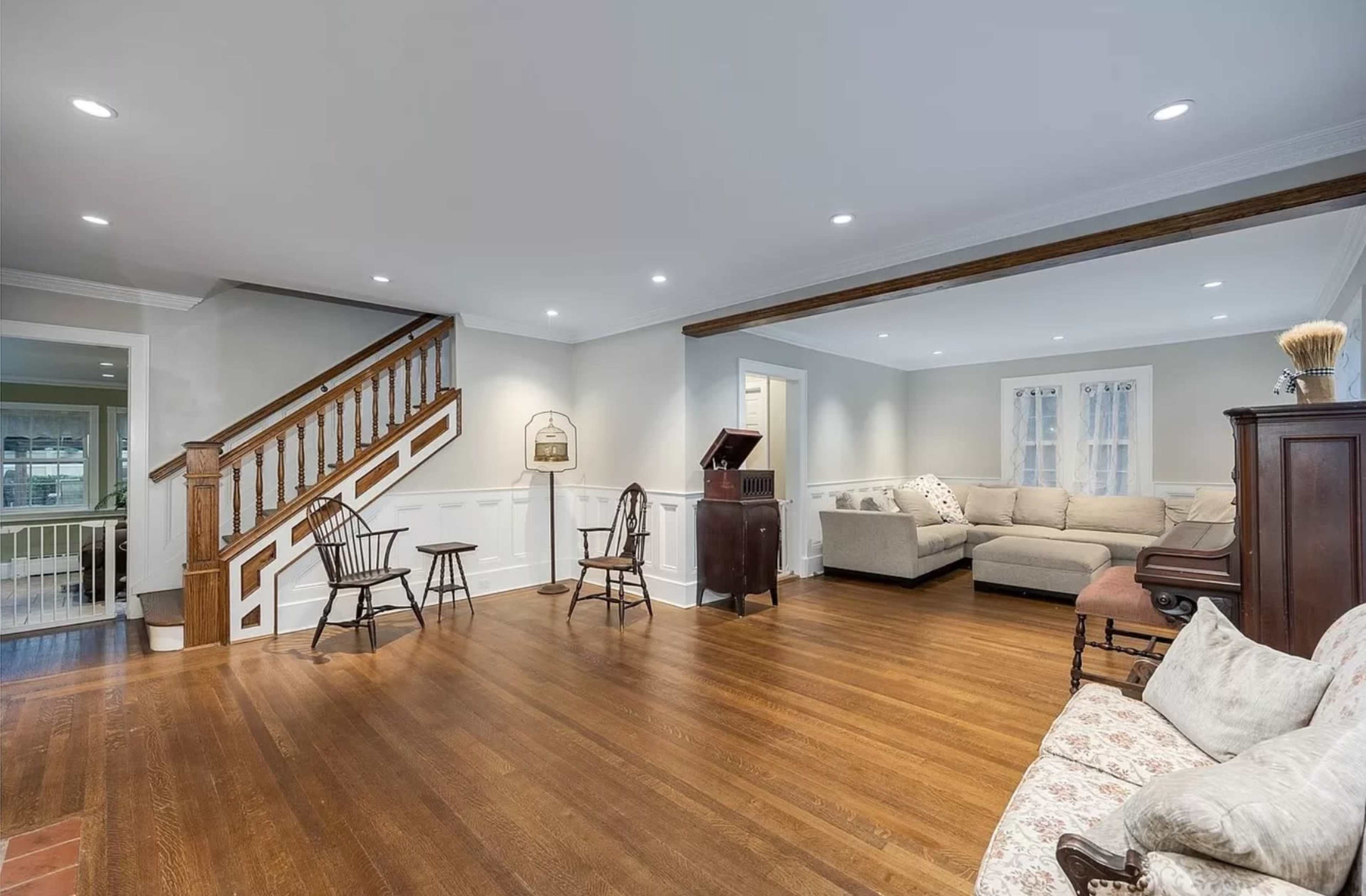 A spacious living room with hardwood flooring, a staircase, and a mix of seating arrangements including chairs and a sofa.