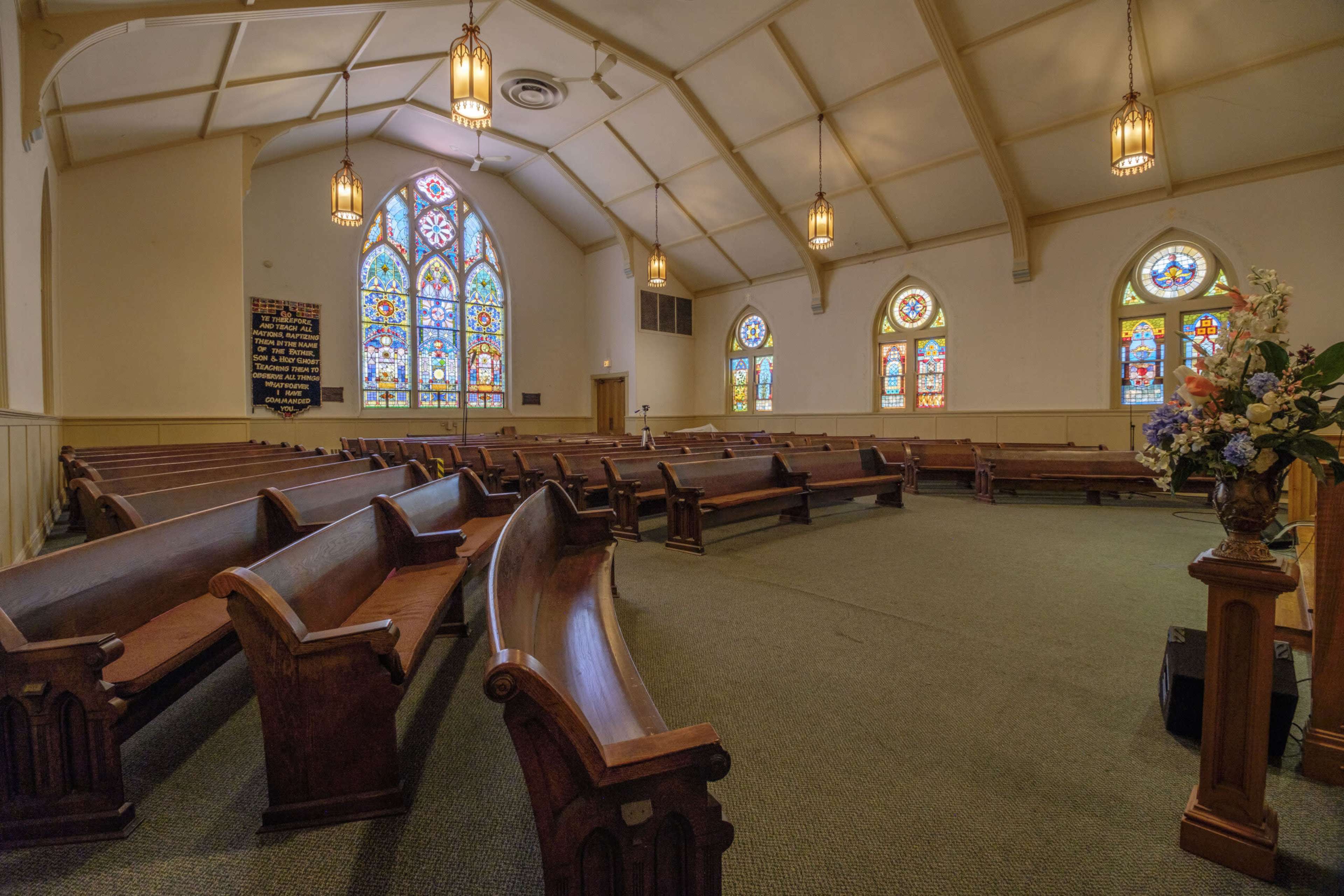 The interior of a church featuring wooden pews and colorful stained glass windows.