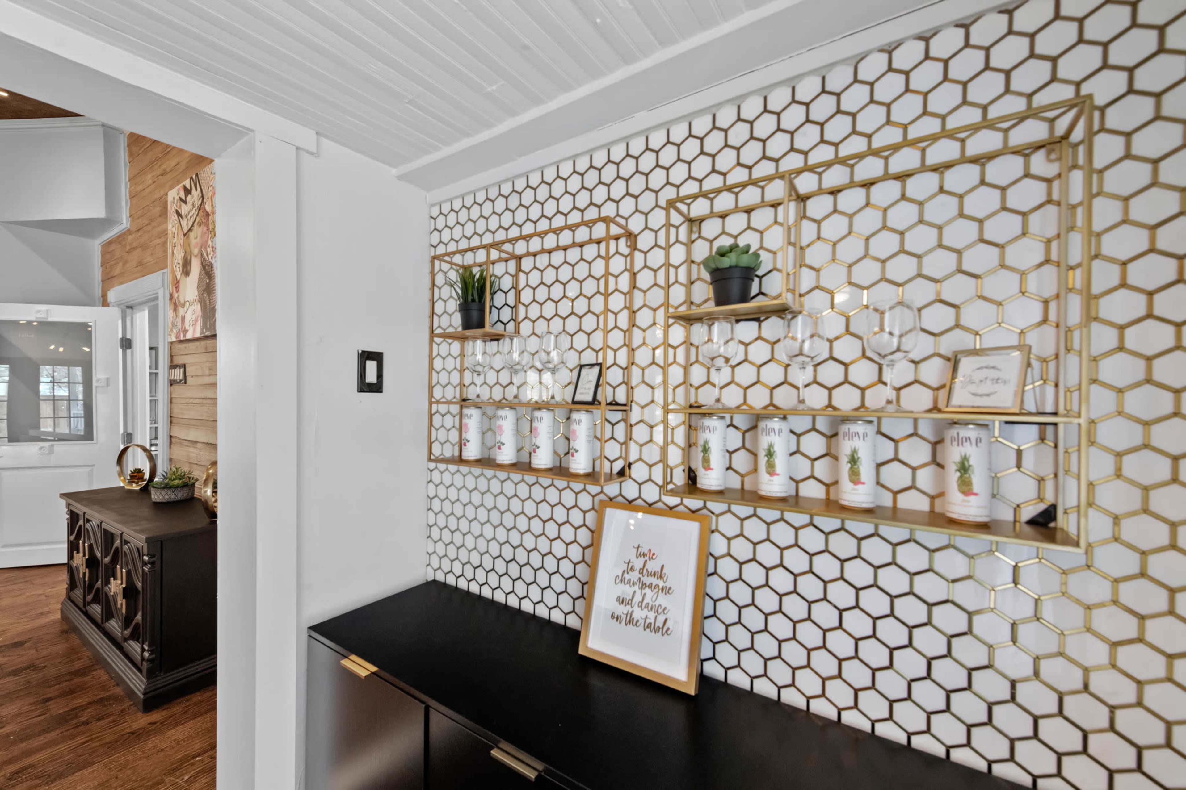 A patterned wall featuring hexagonal tiles with gold shelving units displaying plants and decorative items.