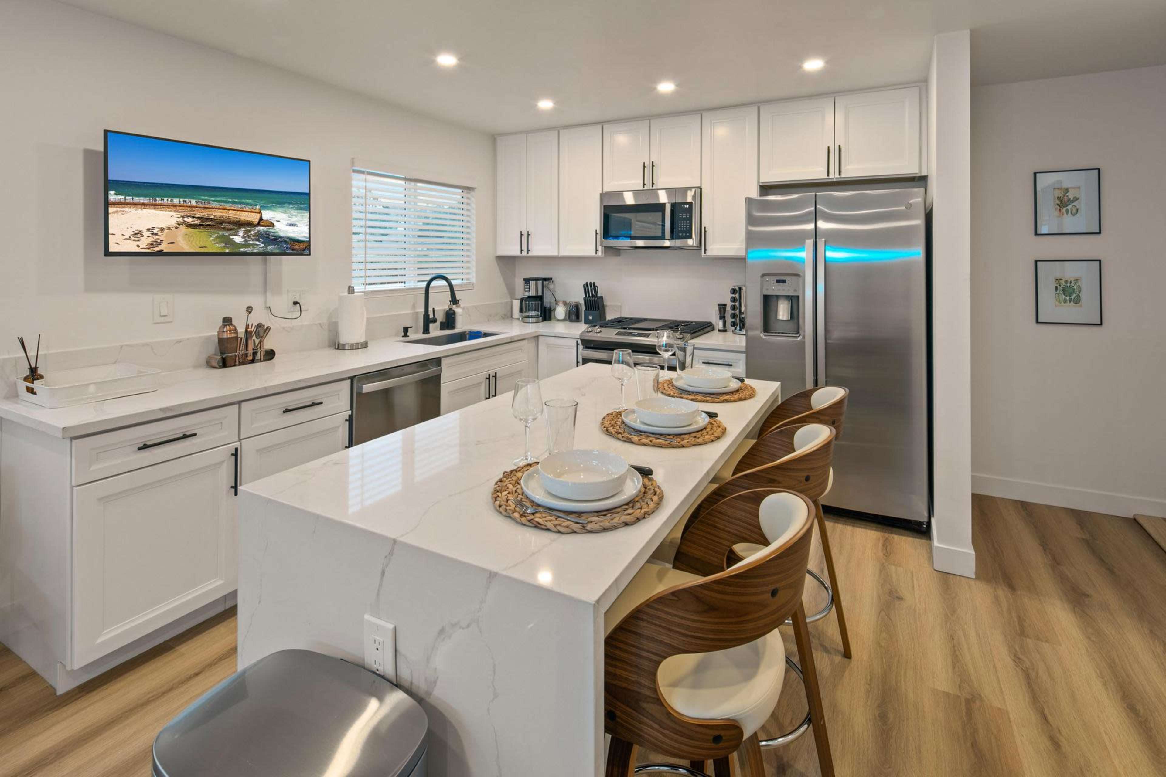 The kitchen features modern appliances, white cabinetry, and a breakfast bar with four stools.