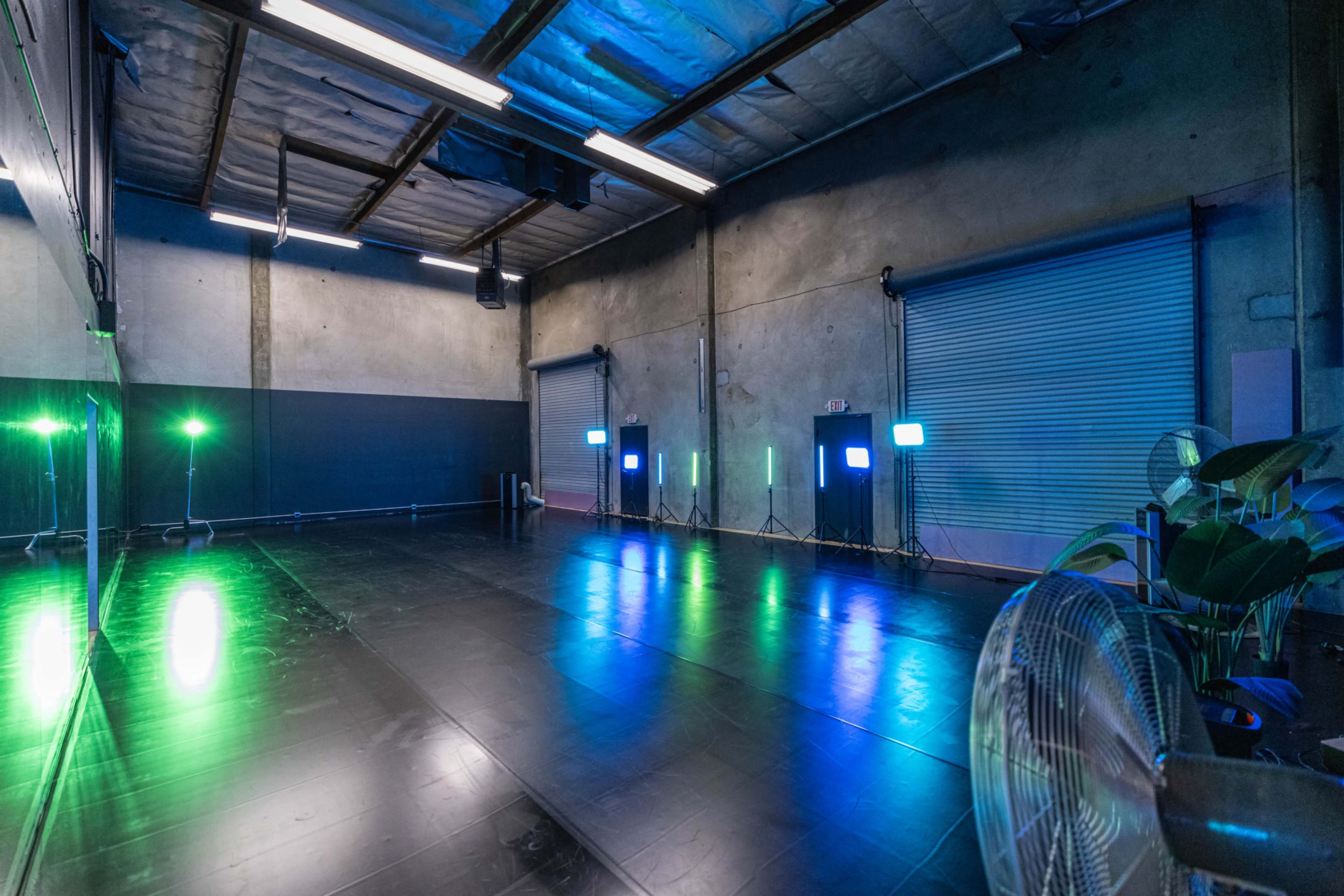 An empty dance studio features a black floor, mirrored wall, and illuminated from behind by colorful lights.