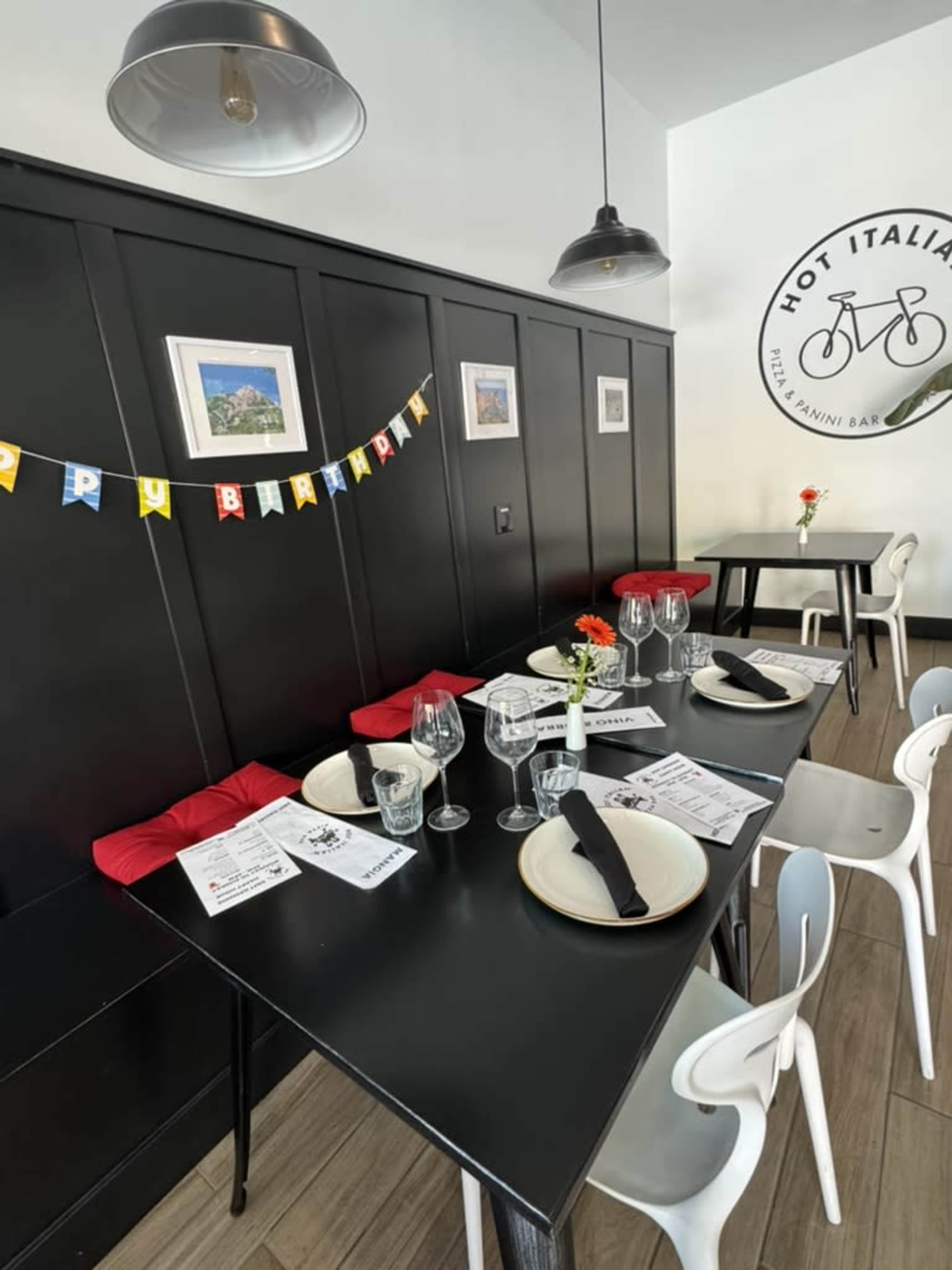 A dining area features a black tabletop set for a celebration, complete with plates, glasses, and a "Happy Birthday" banner.