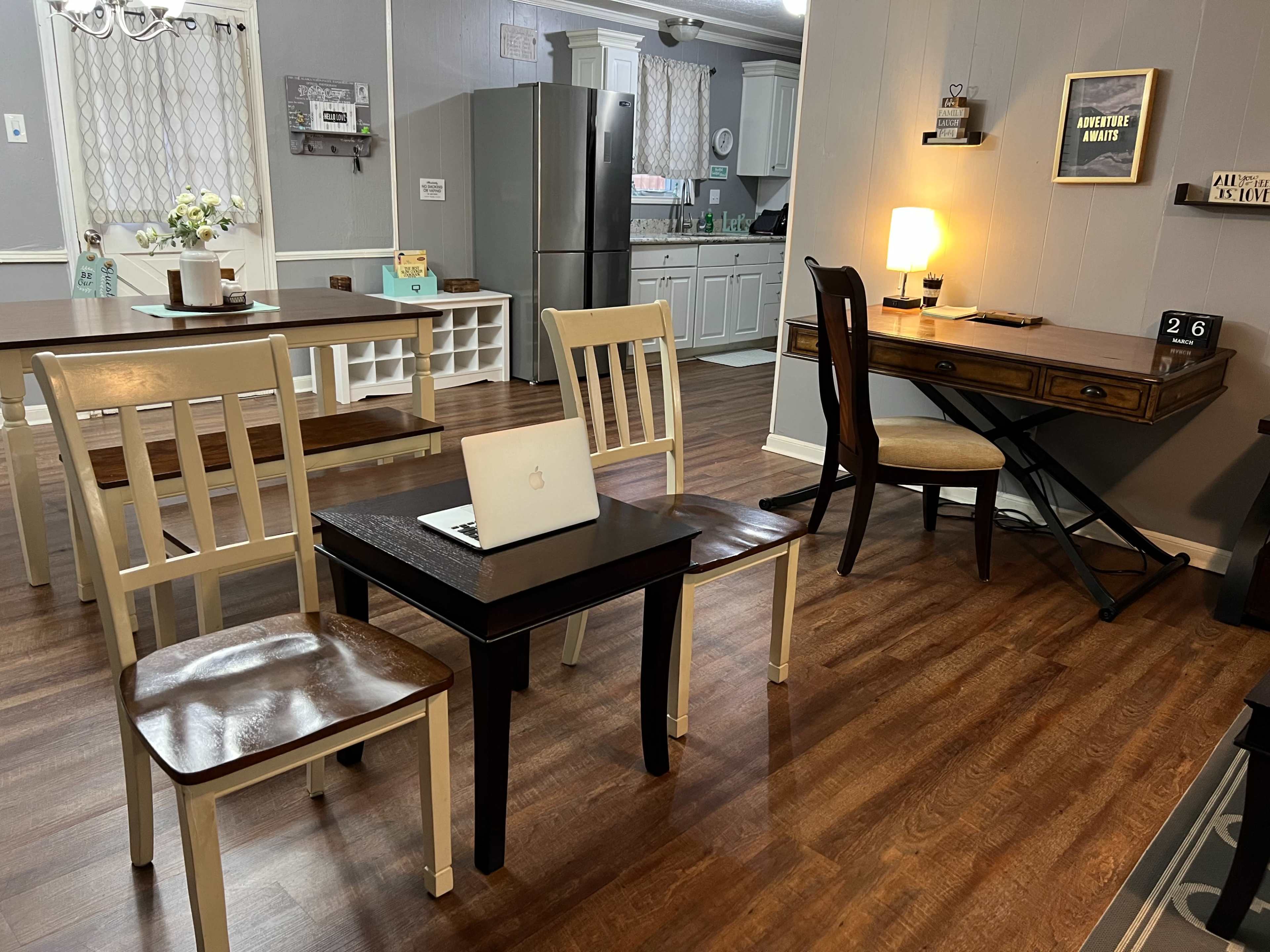 A cozy interior space featuring a small table with a laptop on it, surrounded by three chairs, and a desk with a lamp in the background.